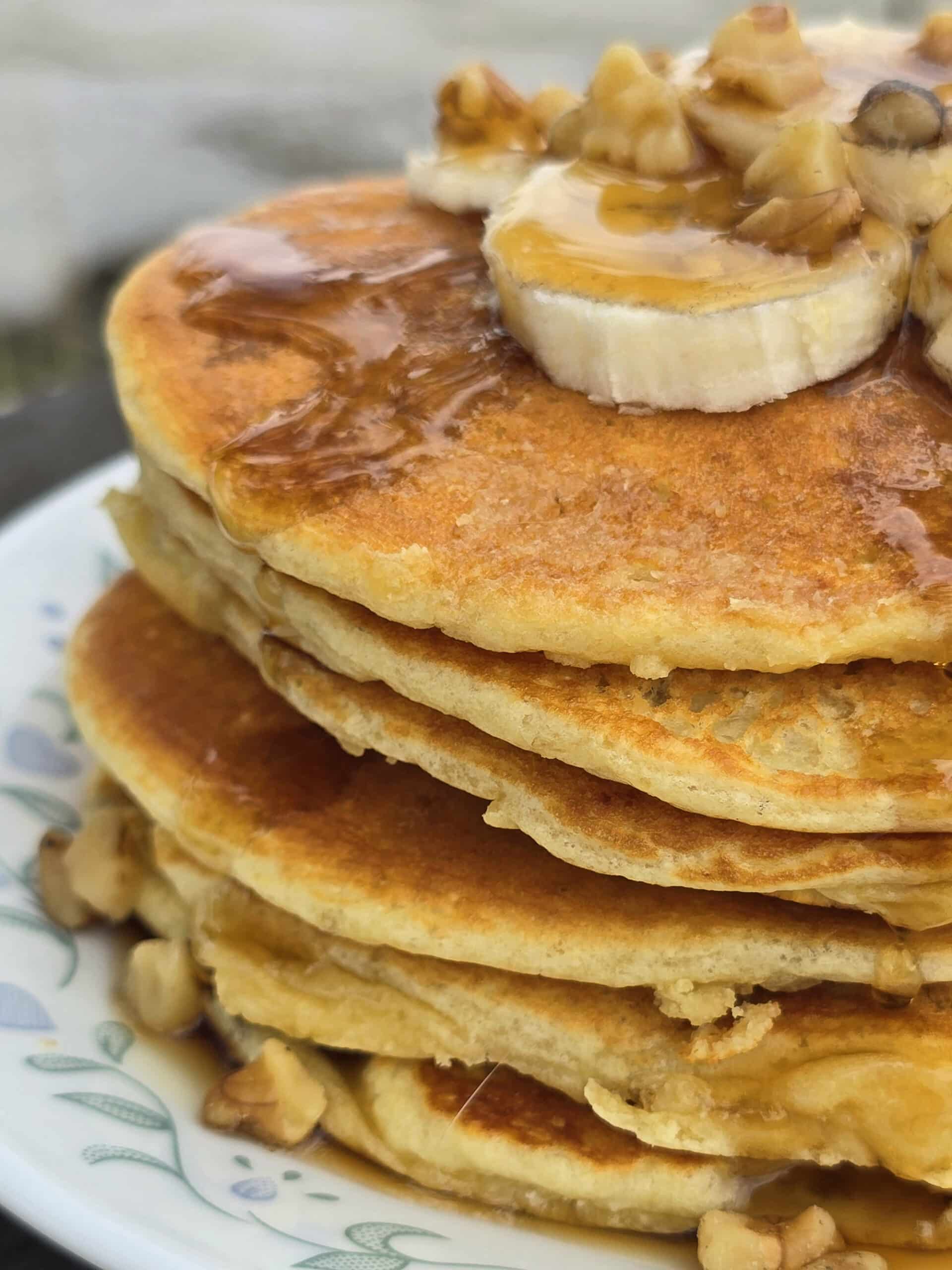 A stack of banana protein pancakes with bananas and maple syrup on top.