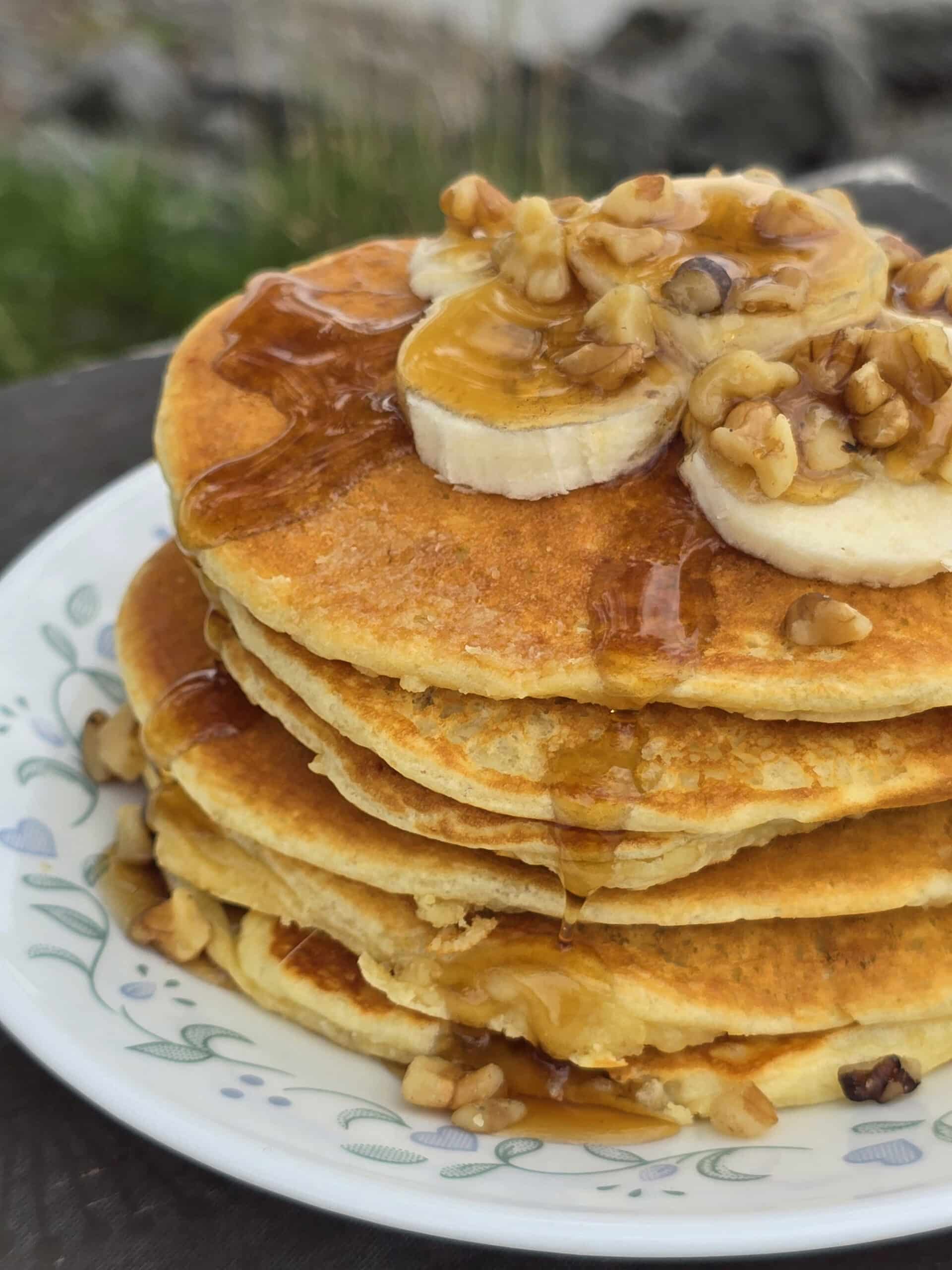 A stack of banana protein pancakes with bananas and maple syrup on top.