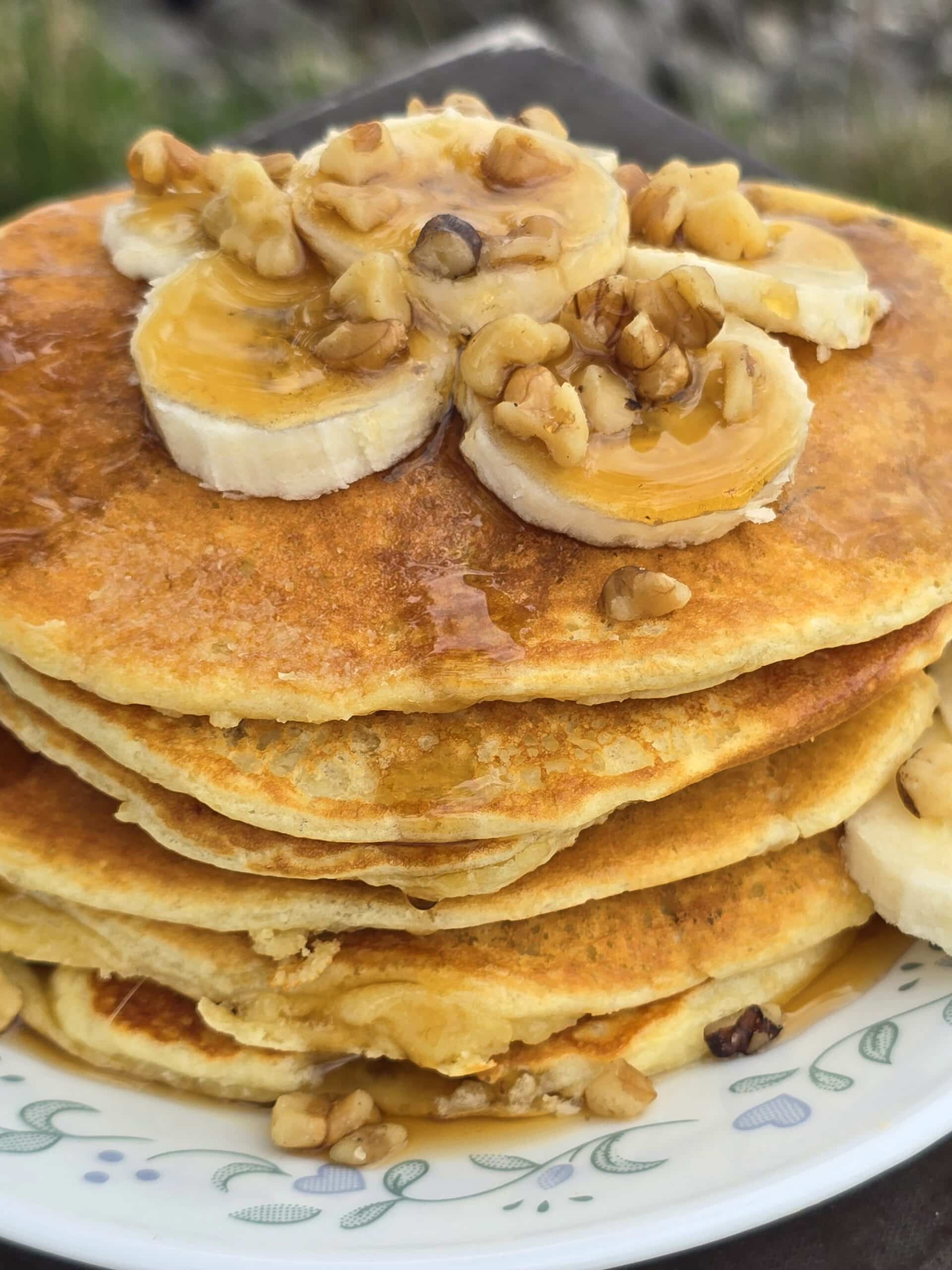 A stack of banana protein pancakes with bananas and maple syrup on top.