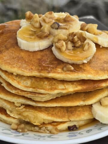 A stack of banana protein pancakes with bananas and maple syrup on top.