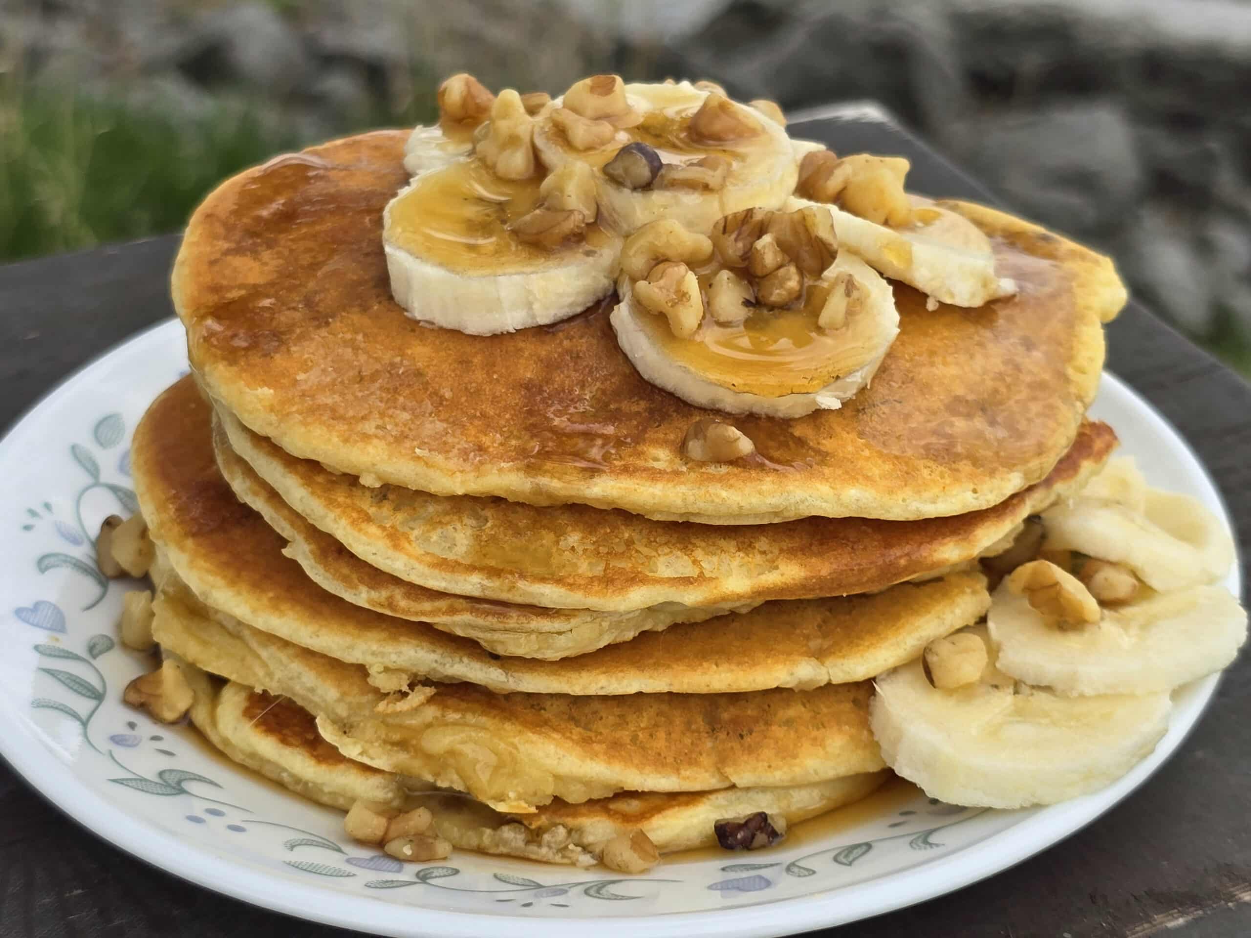 A stack of banana protein pancakes with bananas and maple syrup on top.