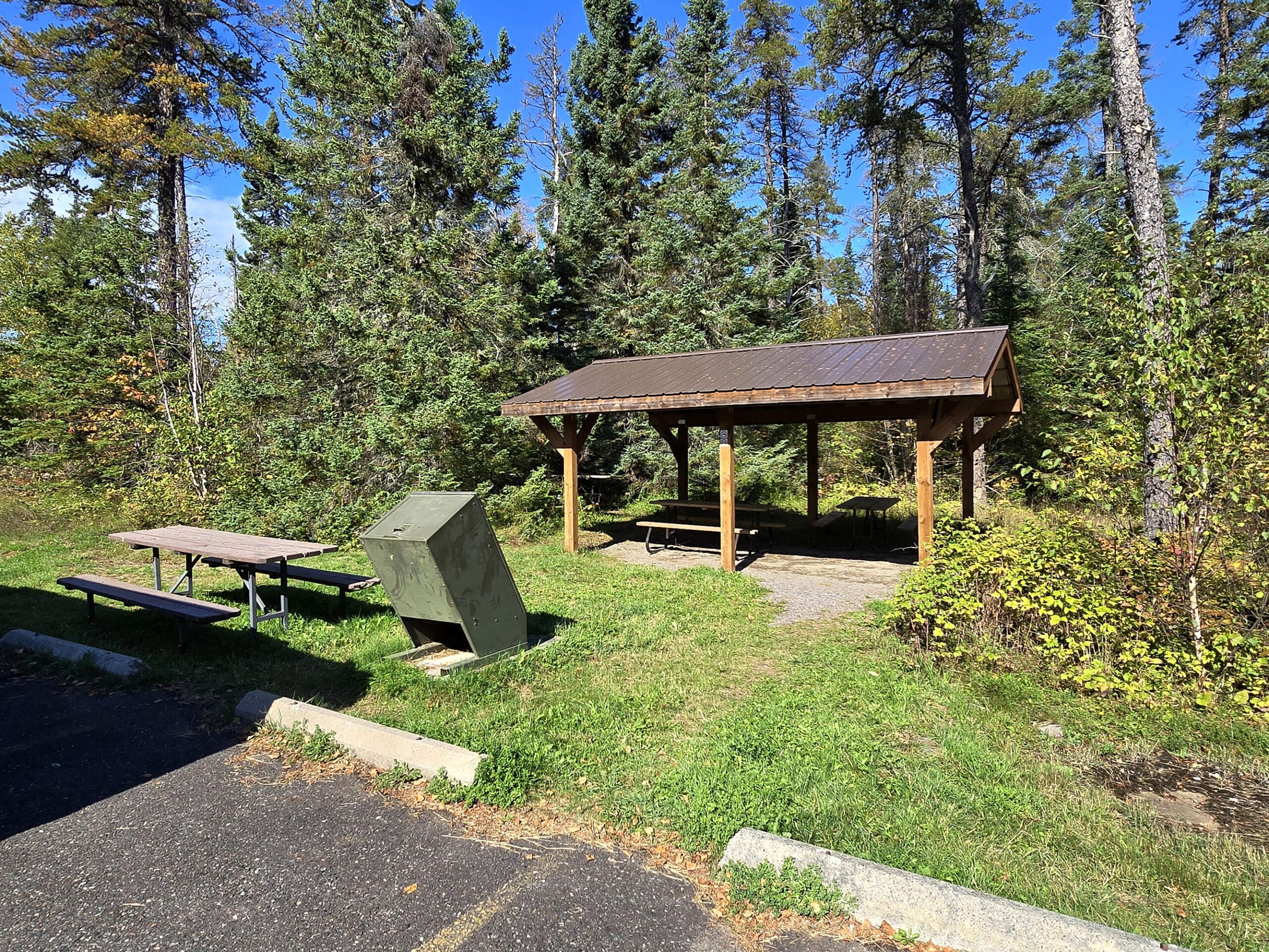 A small picnic shelter and external picnic table on the edge of a parking lot.