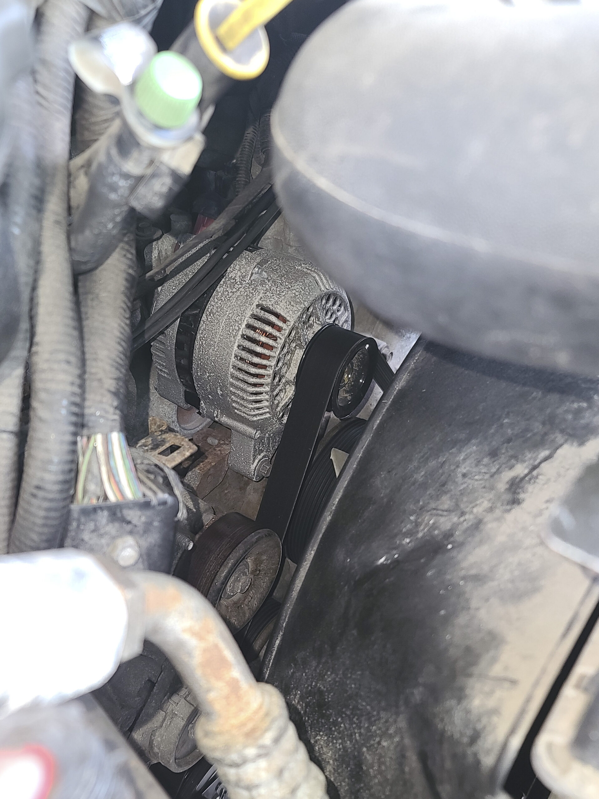 A photo looking under the hood of a motorhome, showing the alternator and belt.