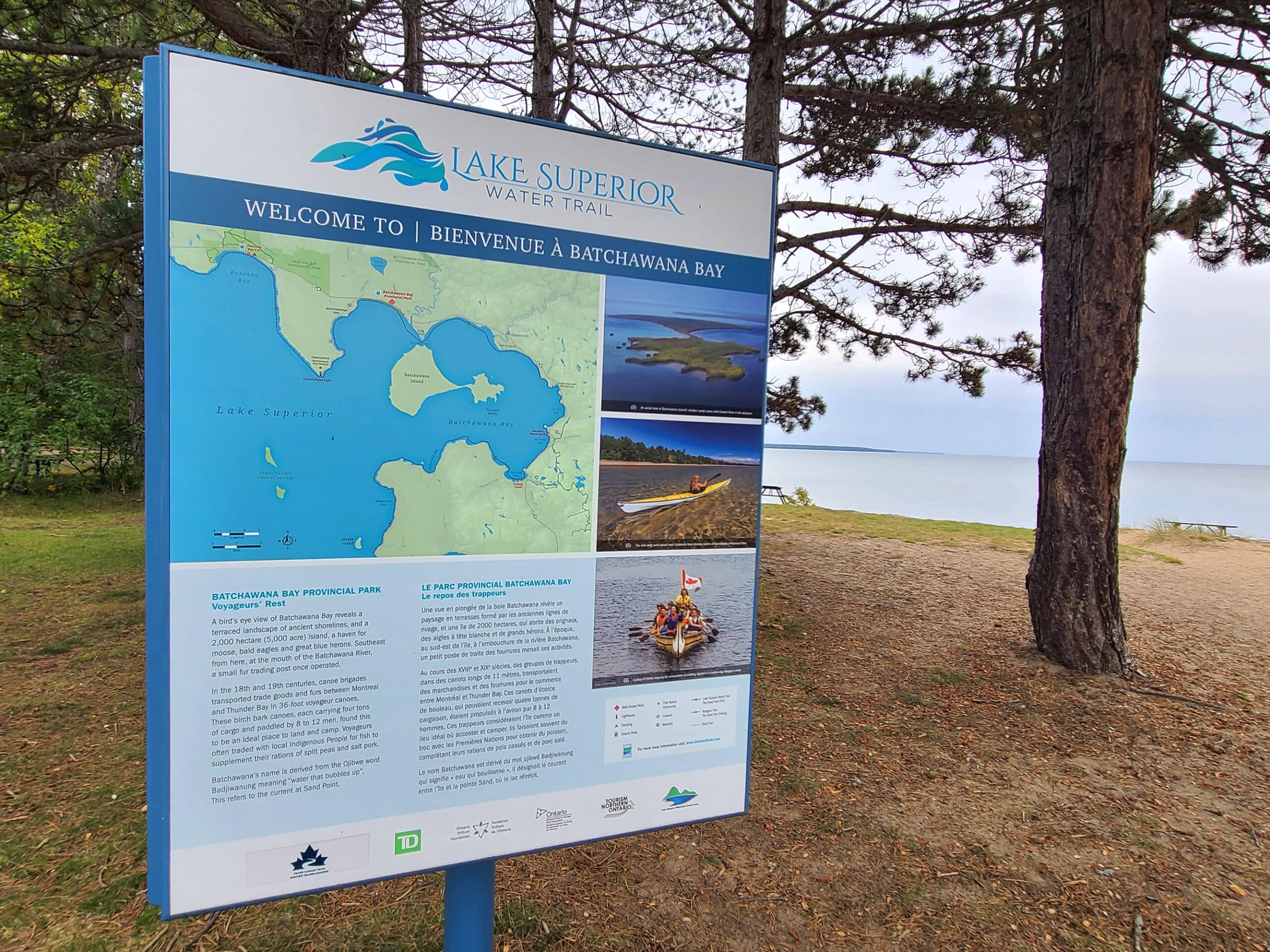 A park sign telling about Batchawana Bay, with the beach in the background.