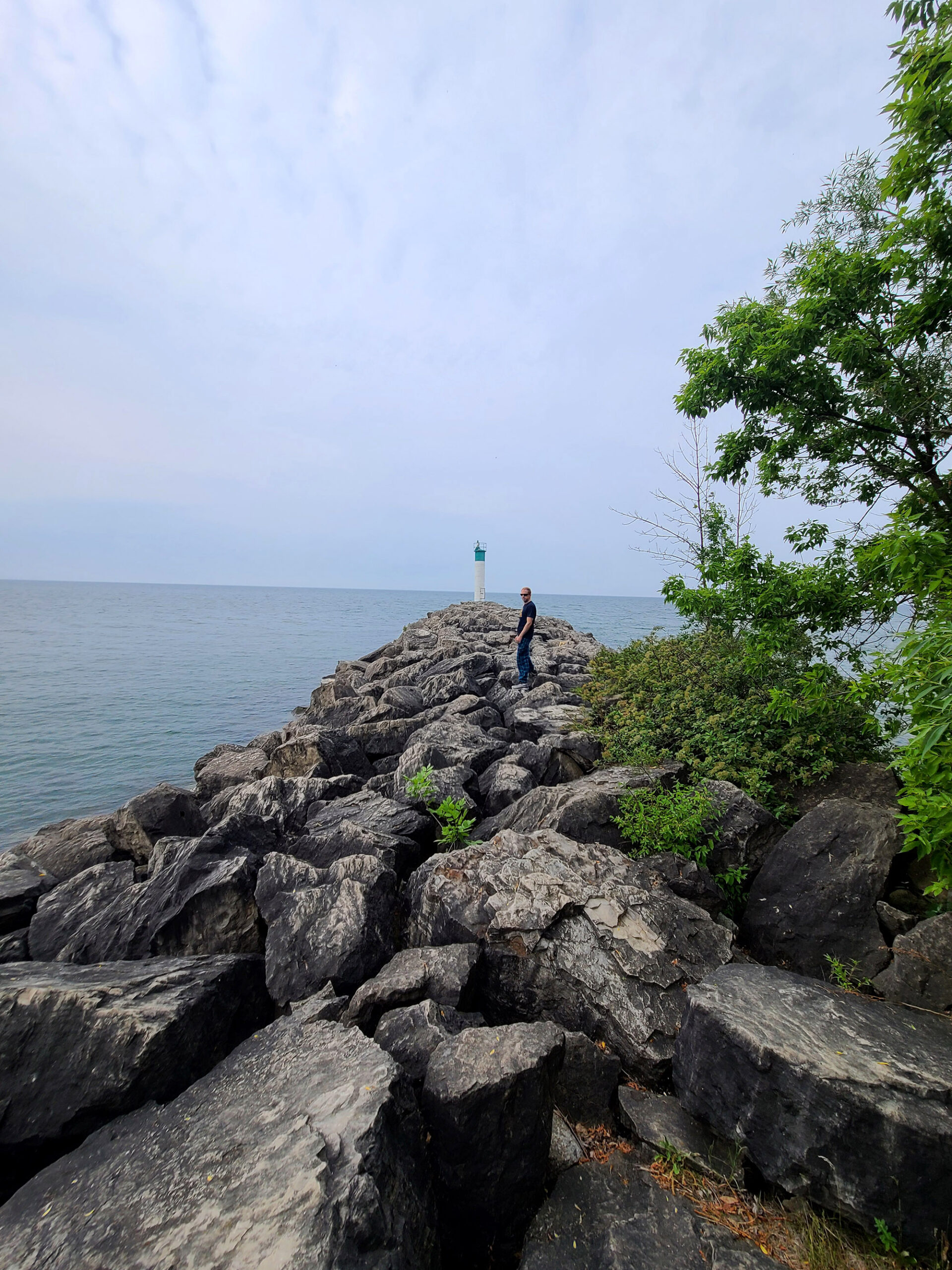 A long pile of boulders jutting out into lake ontario, with a lighthouse in the background.