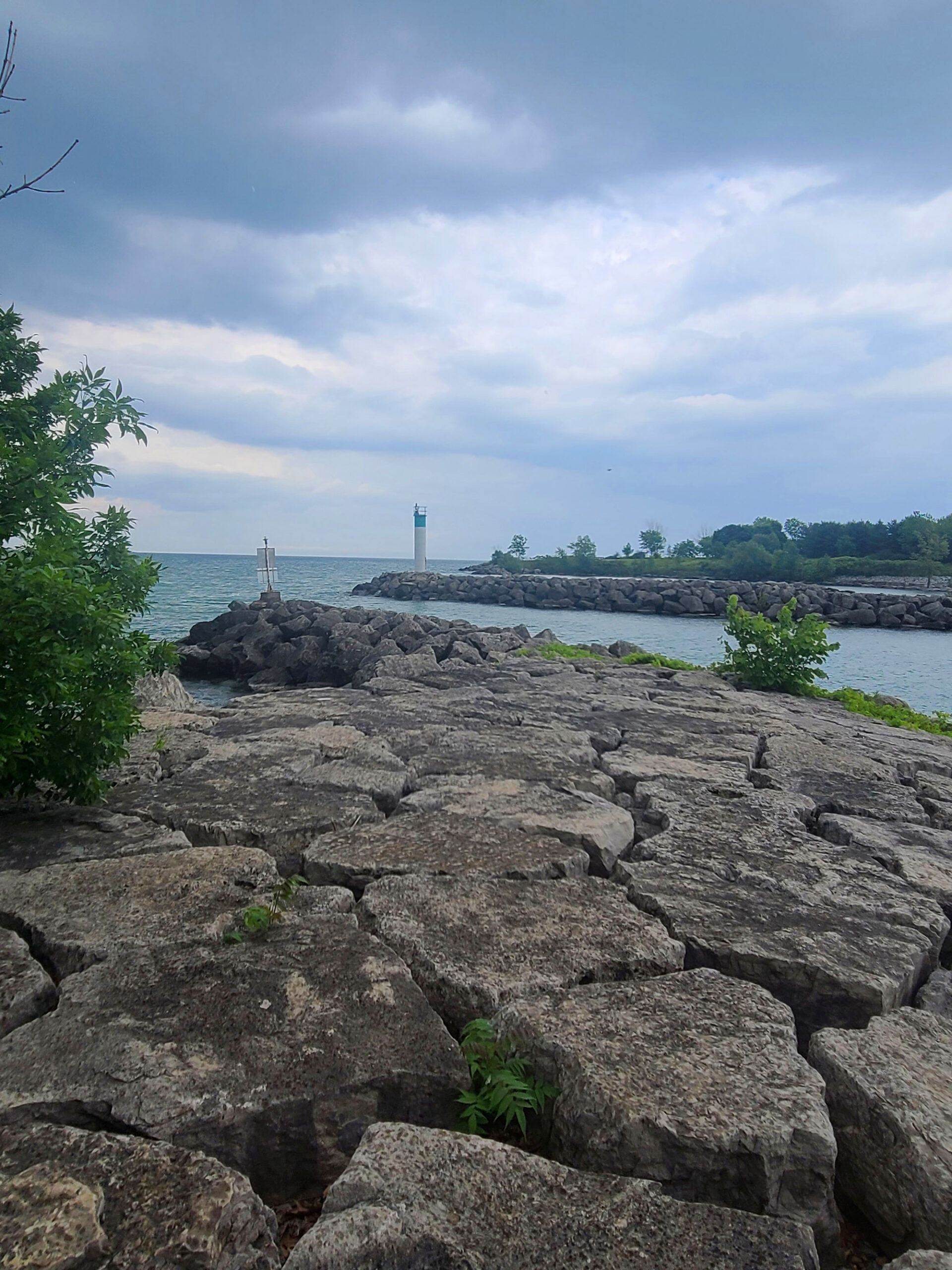 A long pile of boulders jutting out into lake ontario, with a lighthouse in the background.