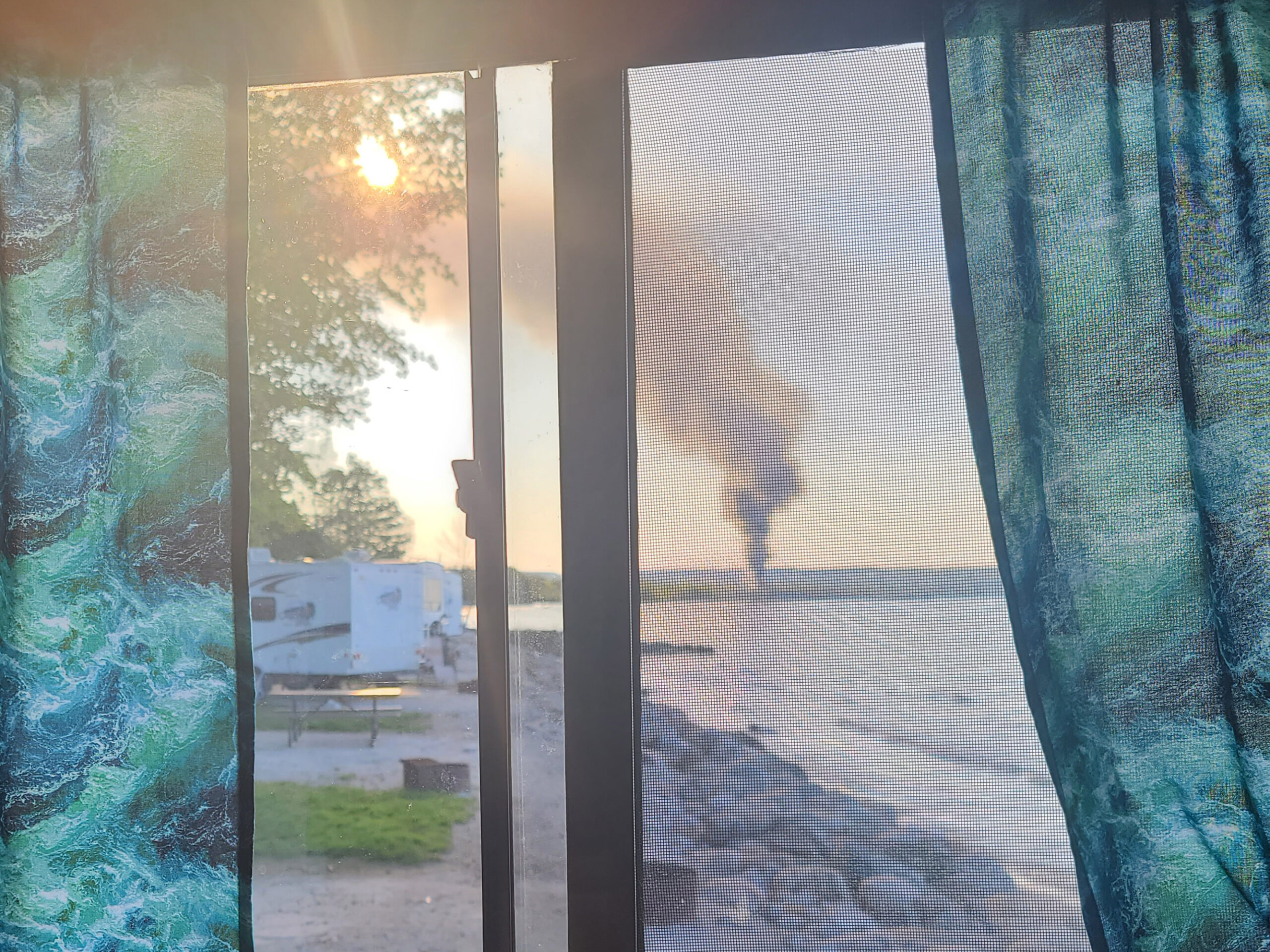 A view of a smoking fire in the distance, across the bay, taken from within an RV camper.