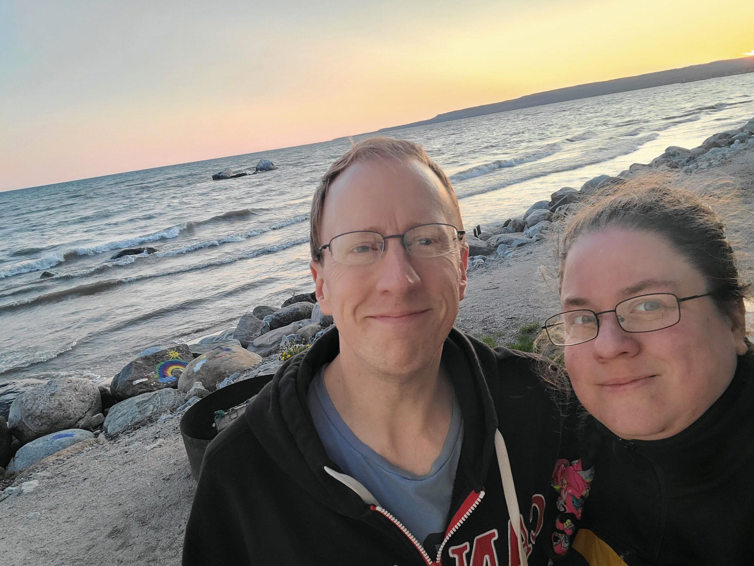 A selfie of a middle aged white couple, with Georgian Bay and the sunset behind them.