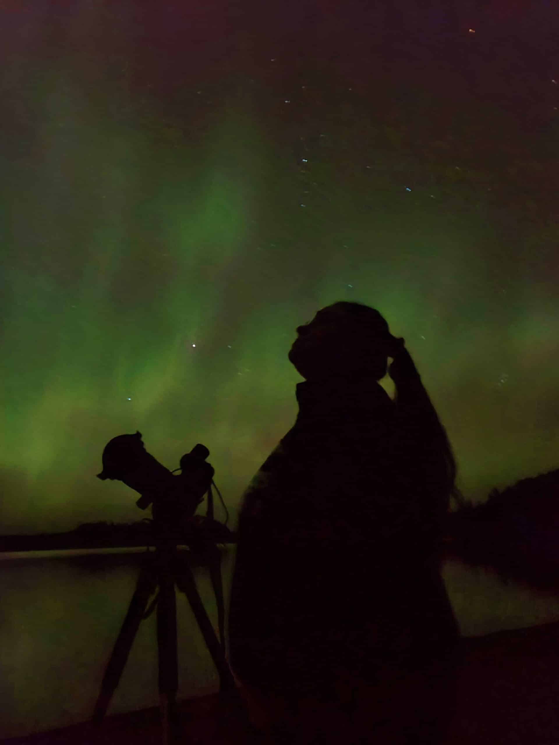 The silhouette of a woman with green northern lights behind her.