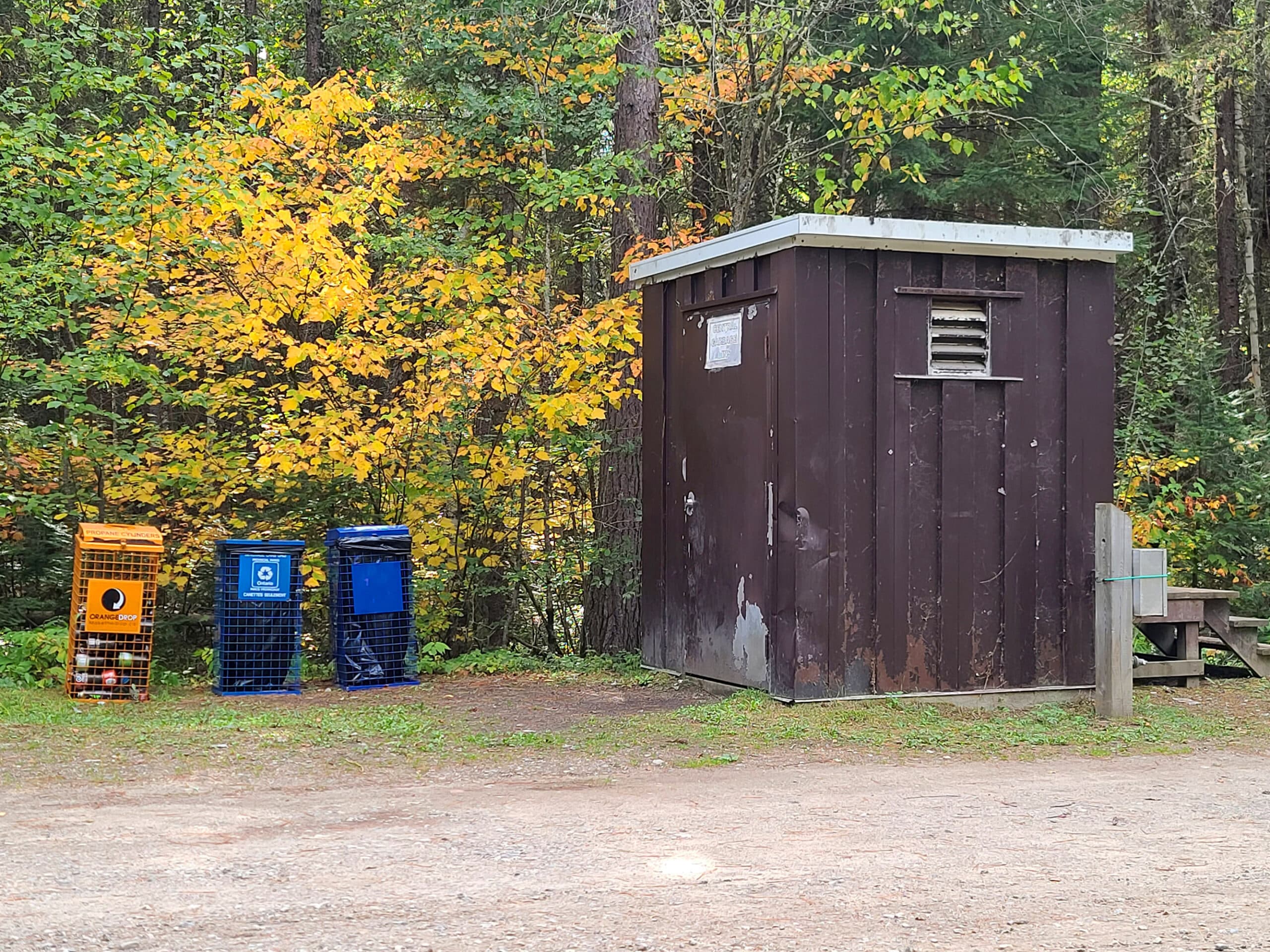 A brown hut for garbage, with 2 smaller recycling bins next to it.
