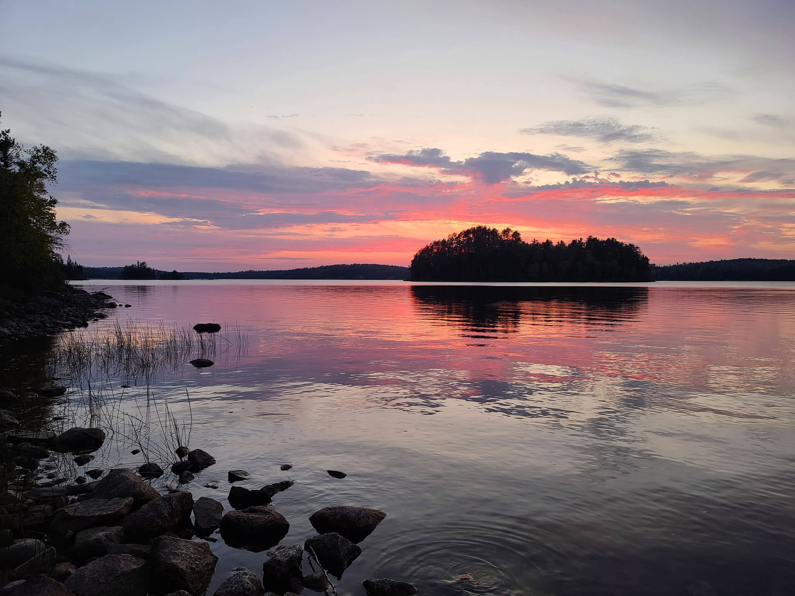 A pink and purple sunset over a lake in quetico provincial park, with an island in the background.