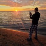 The sun rising over turkey point beach. A man in the foreground is photographing the sunrise.