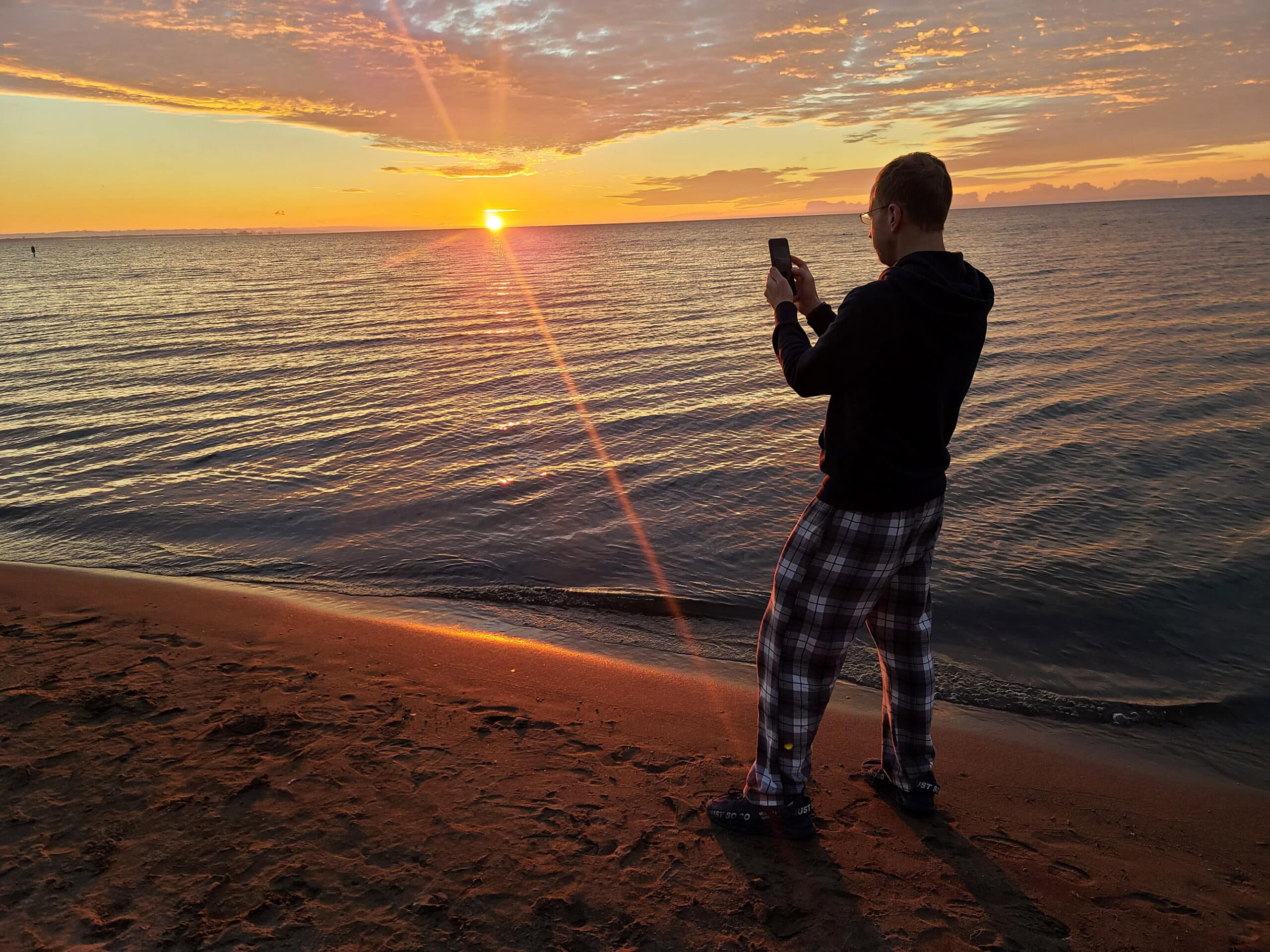 The sun rising over turkey point beach. A man in the foreground is photographing the sunrise.