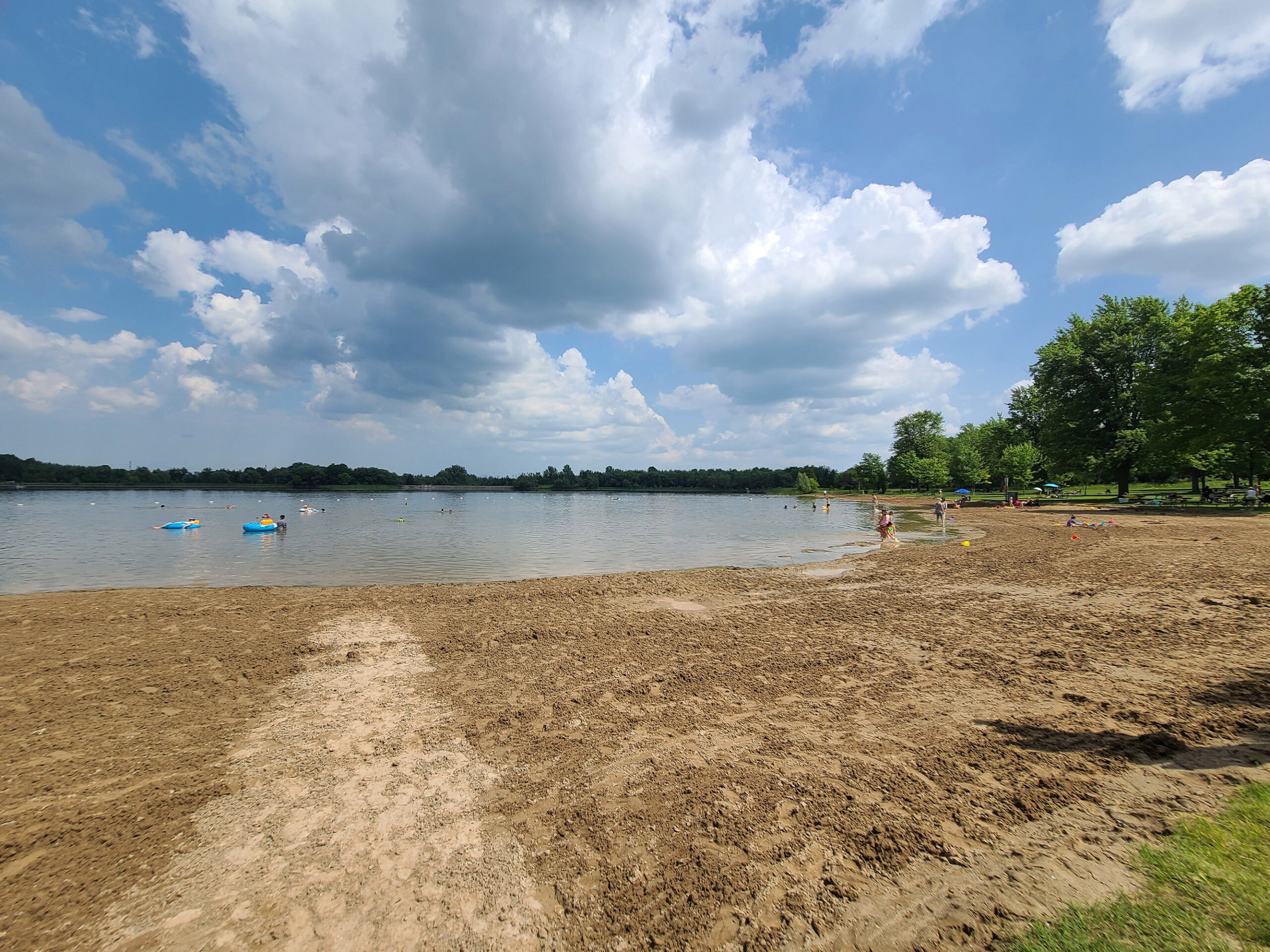 A long, wide sandy beach, There are a few people playing in the water.