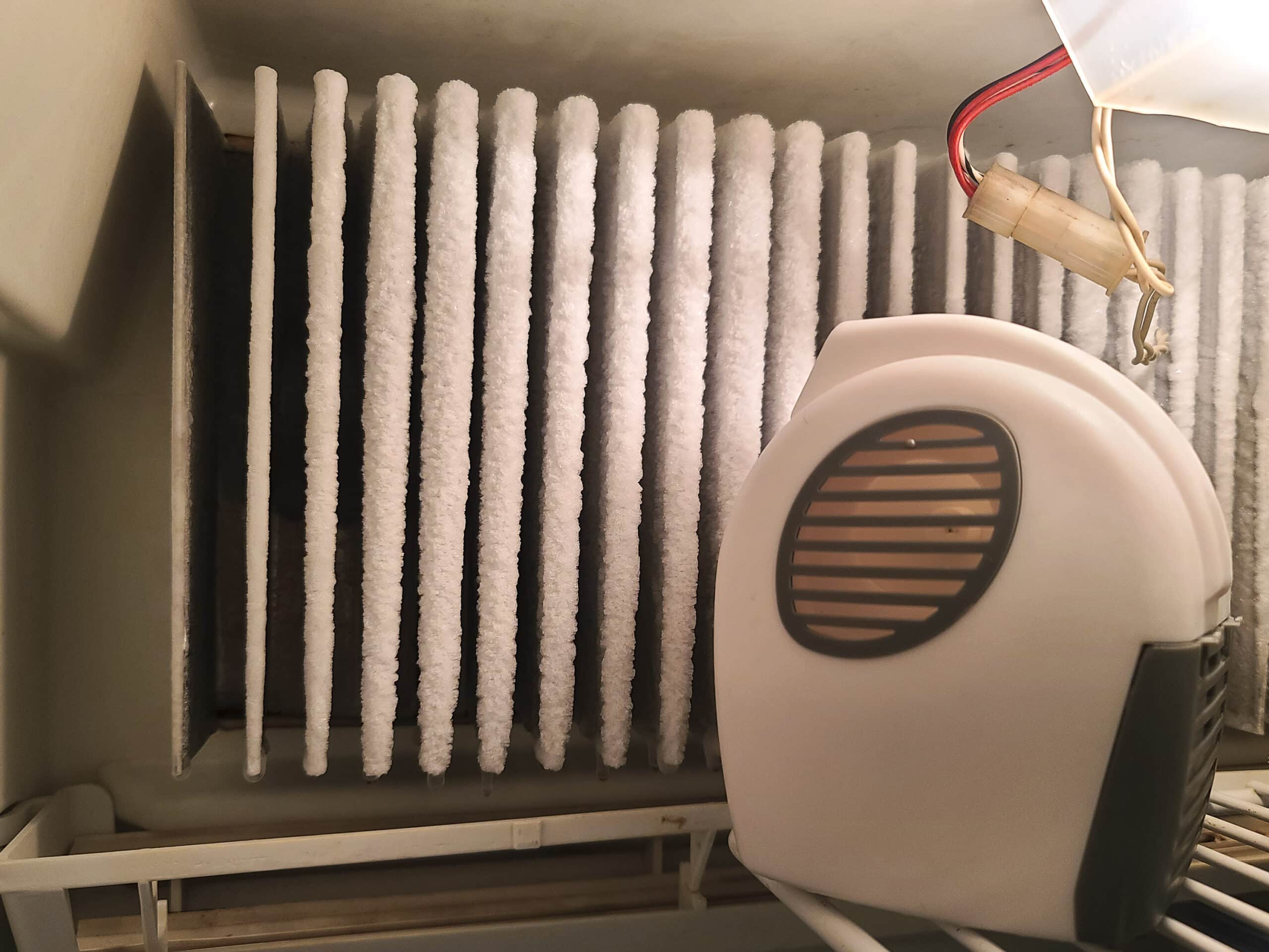 The inside of an RV fridge with a small fan aimed at the fins.  There is ice buildup on the fins.