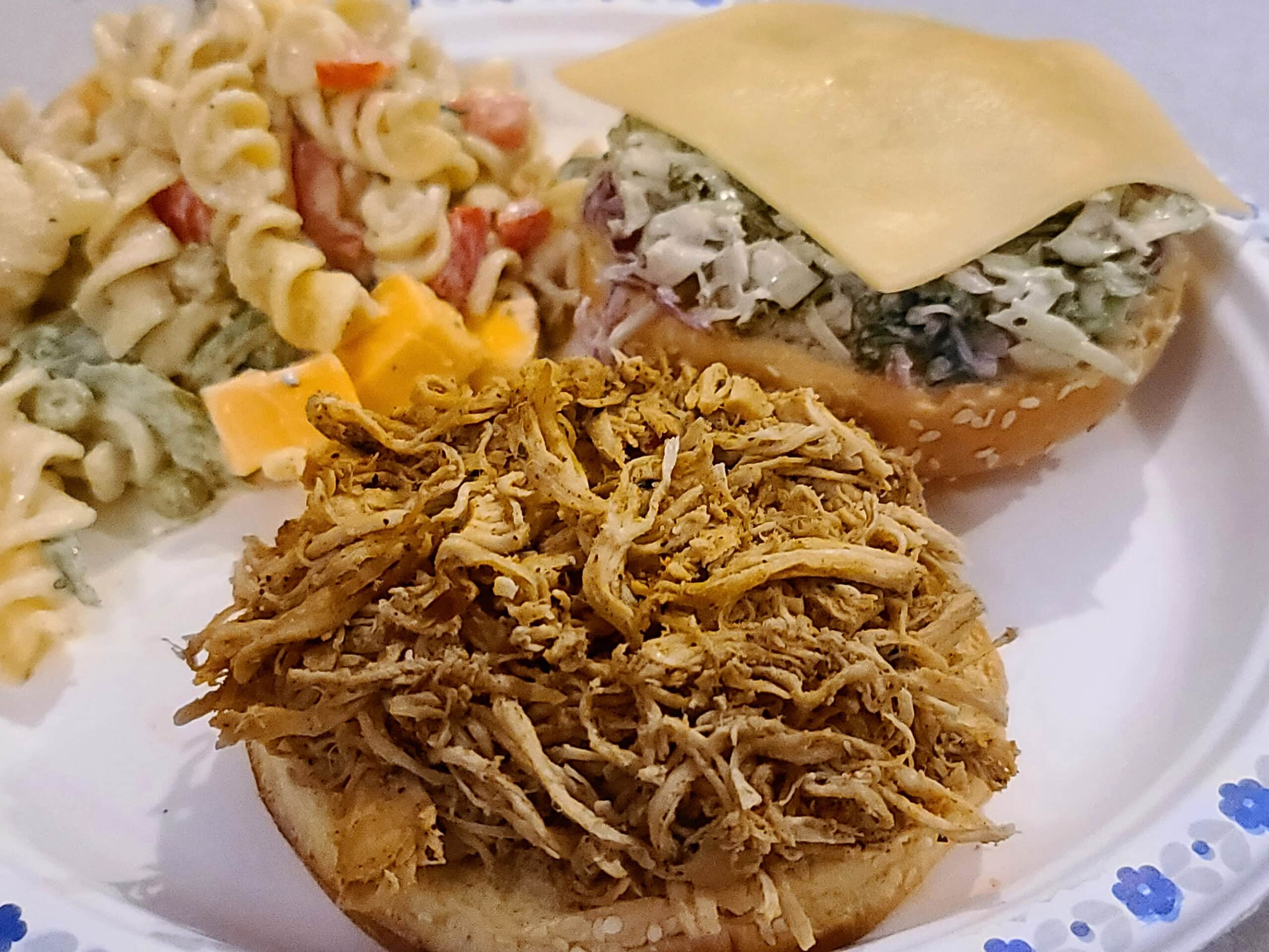 A BBQ pulled chicken sandwich on a plate with macaroni salad.