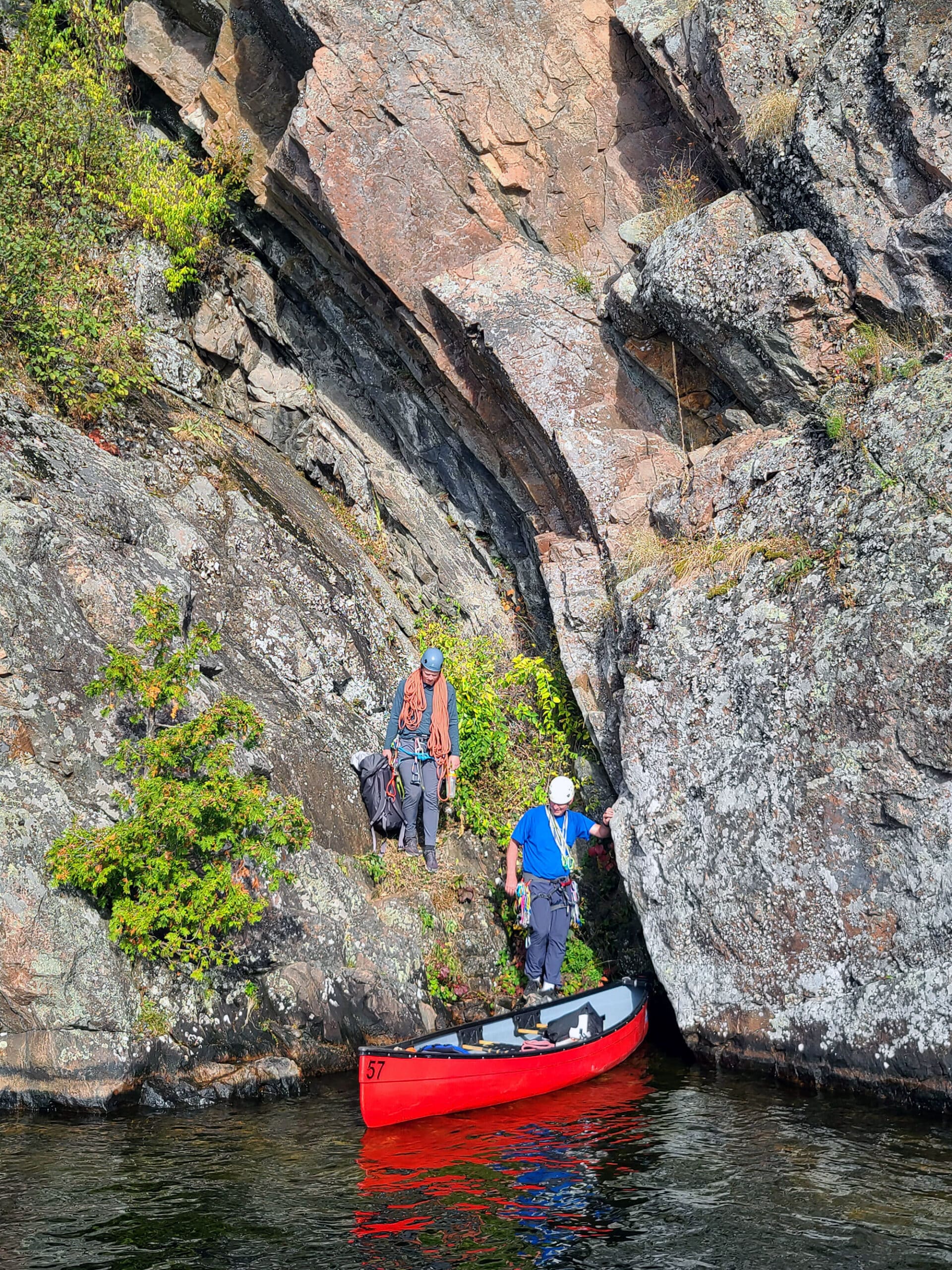 2 rock climbers getting into a red canoe at the bottom of mazinaw rock.