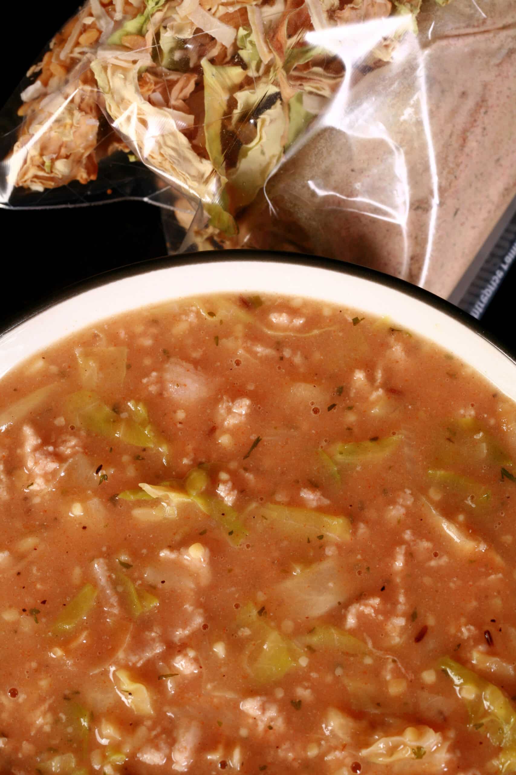 A bowl of cabbage roll soup, in front of a packet of homemade instant soup mix.