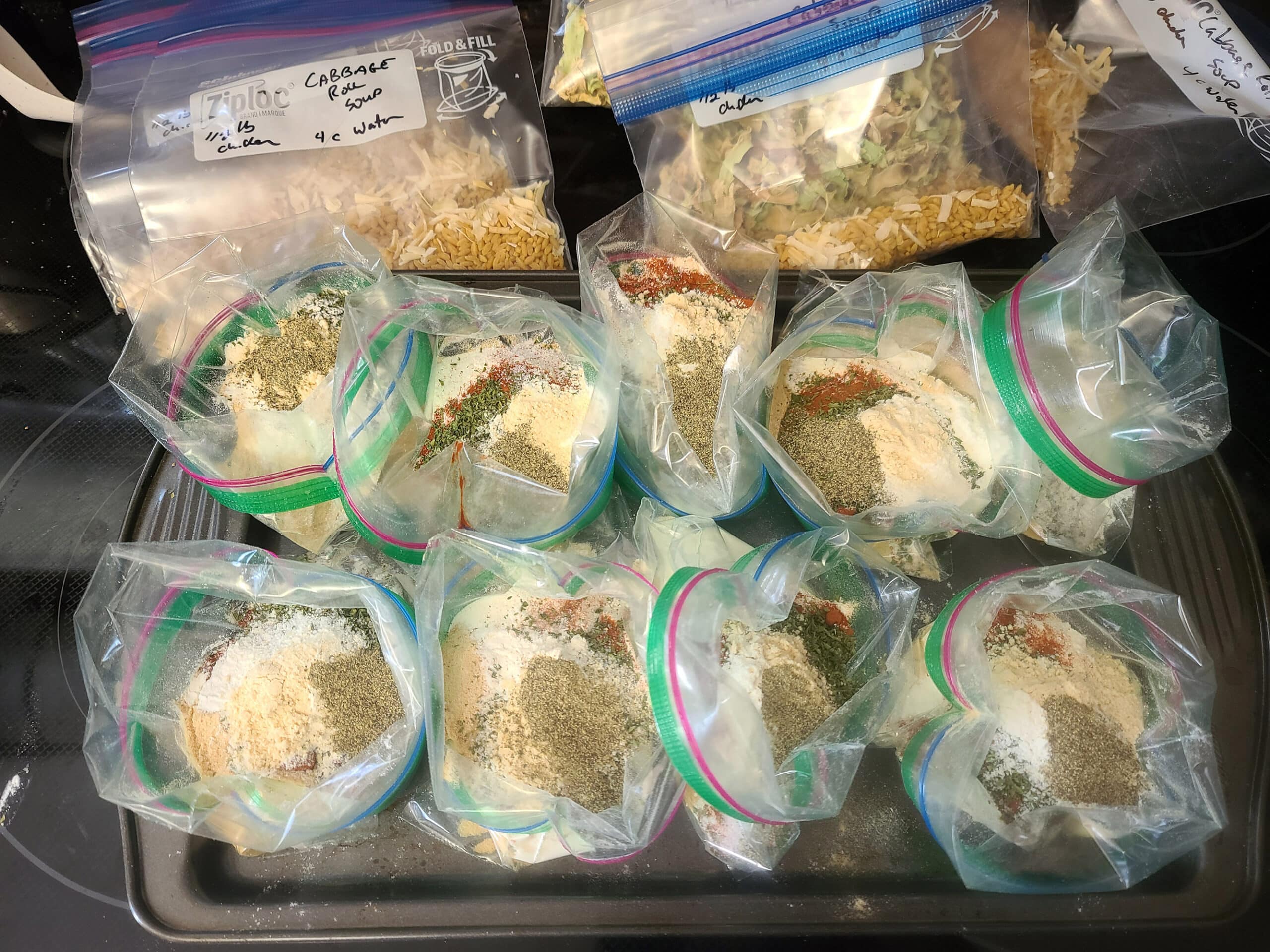 A baking tray set up with 10 baggies, each being filled with the instant soup powder ingredients.