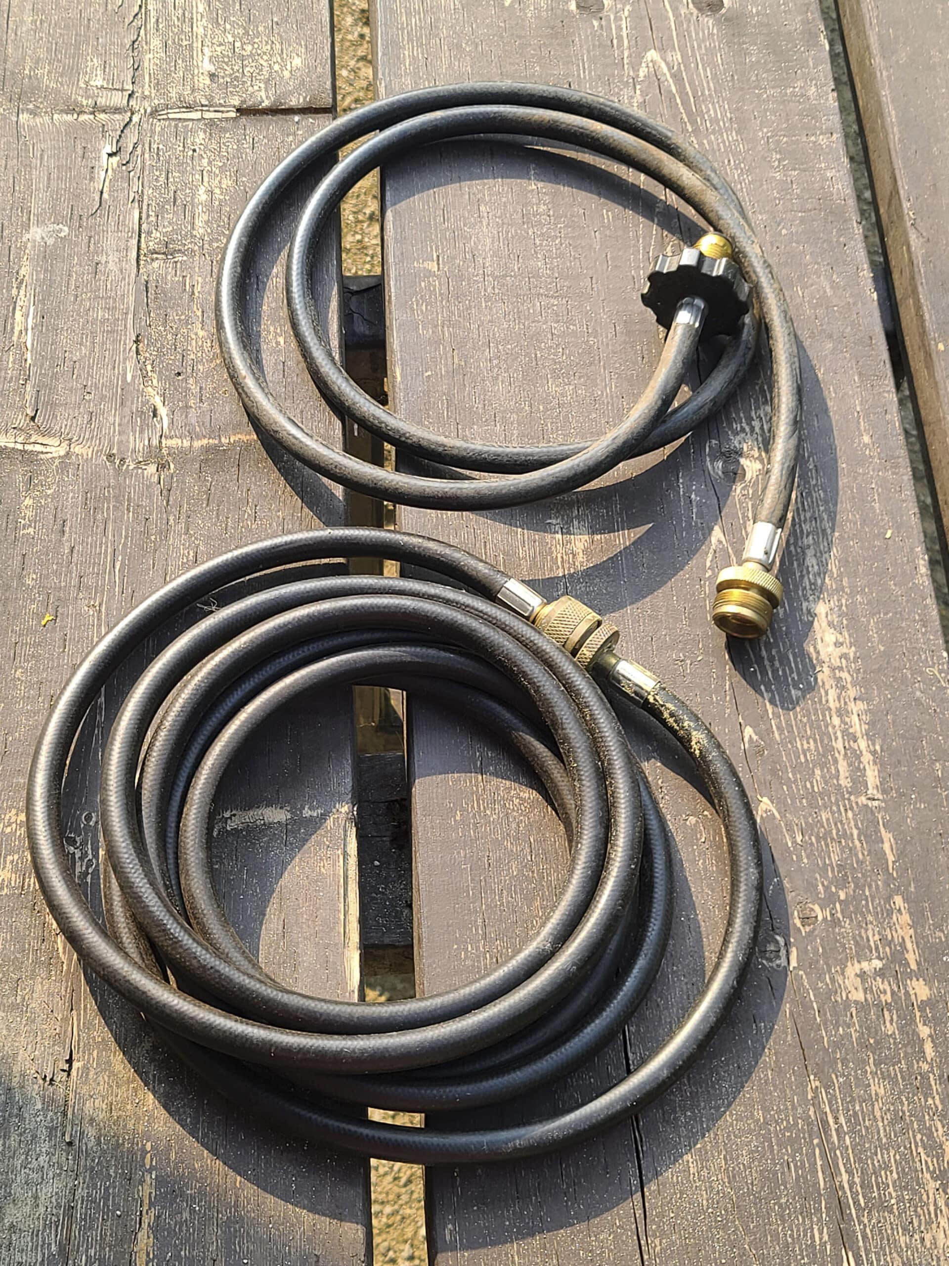 Two black propane hoses are on a table, each coiled up and not connected to anything.