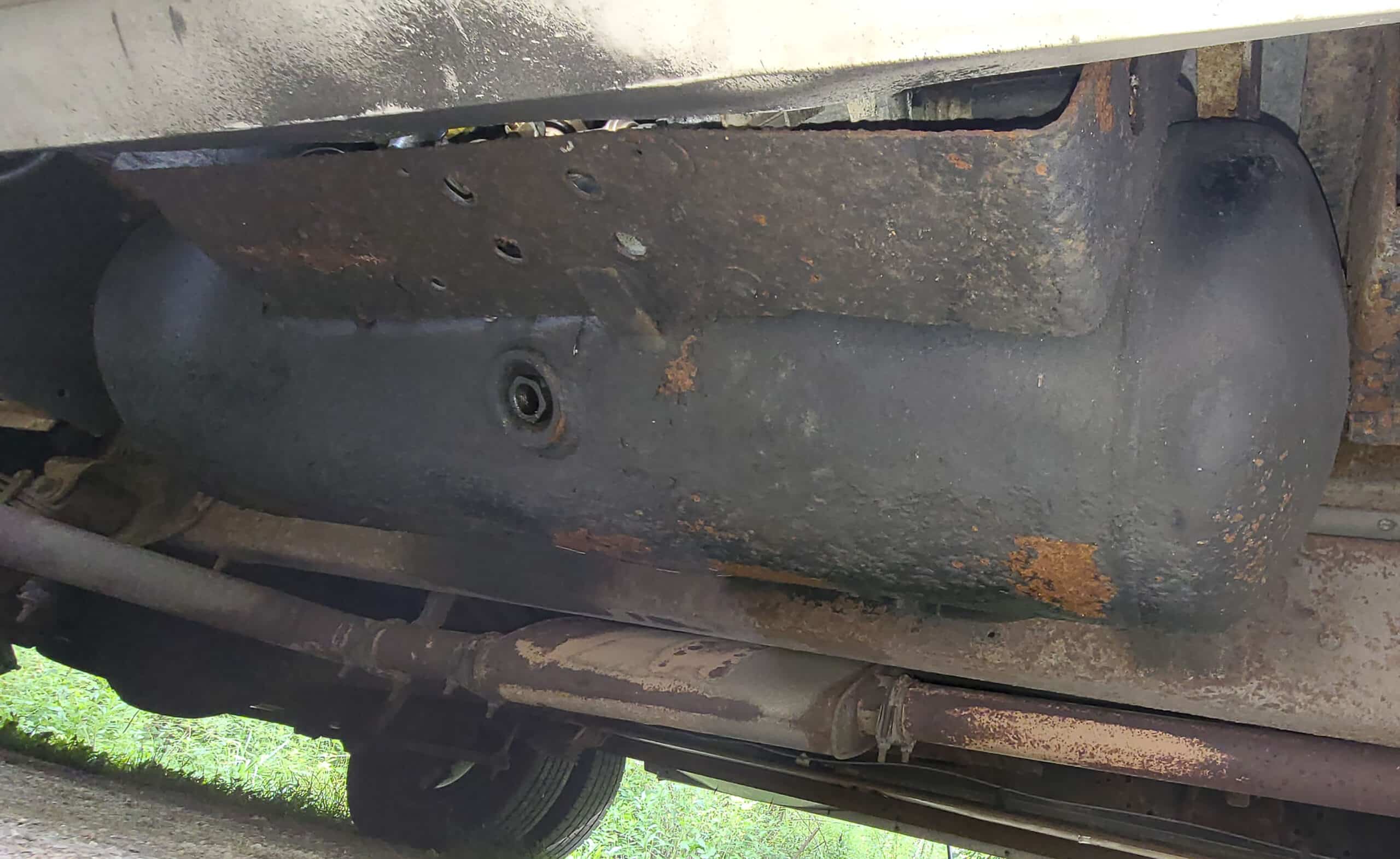 A view under a motorhome.  A large black cylindrical propane tank is seen.  There is minor surface rust in one section.