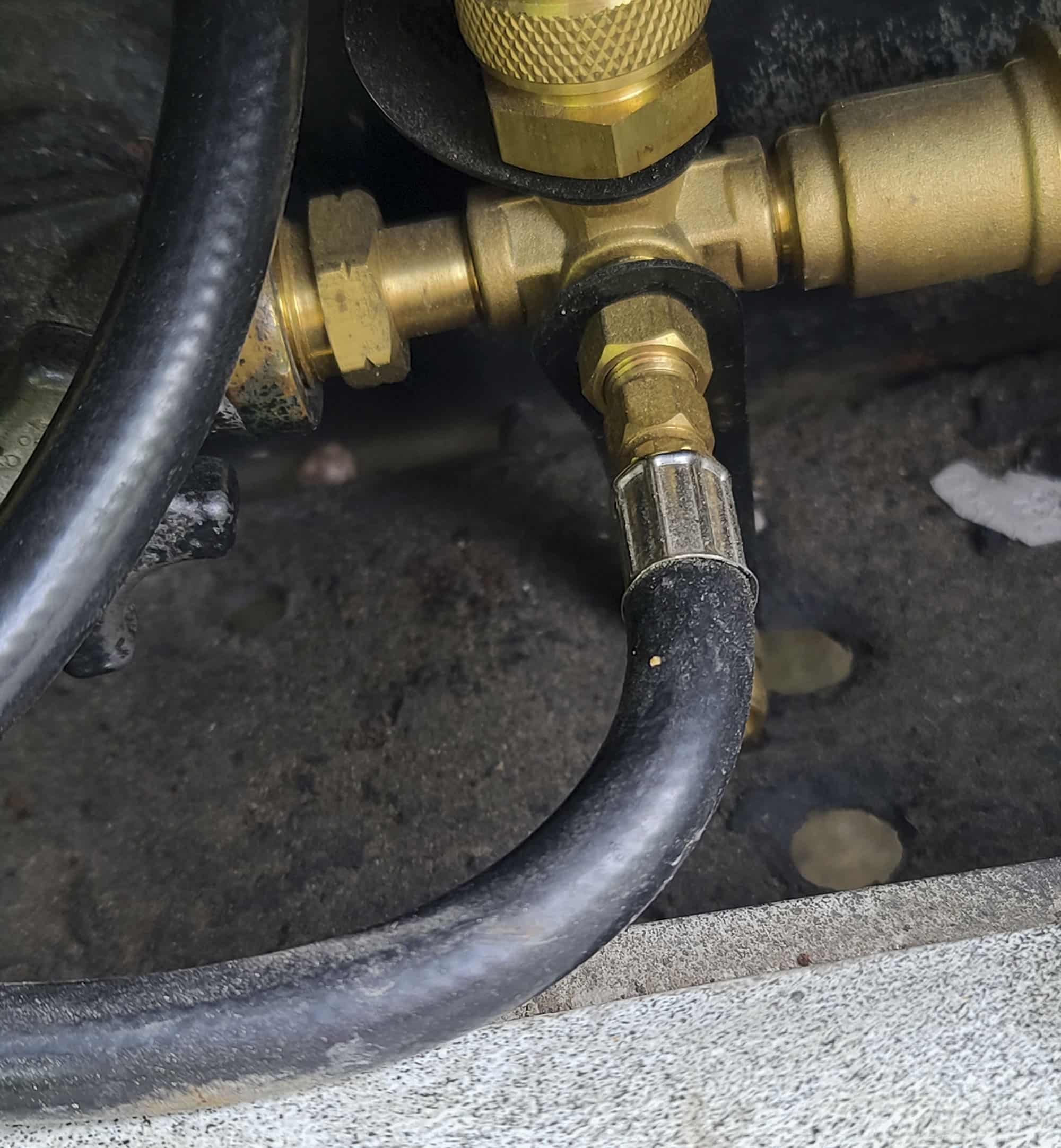A small black propane hose is seen connected to a brass fitting.  The hose is curved to the left.