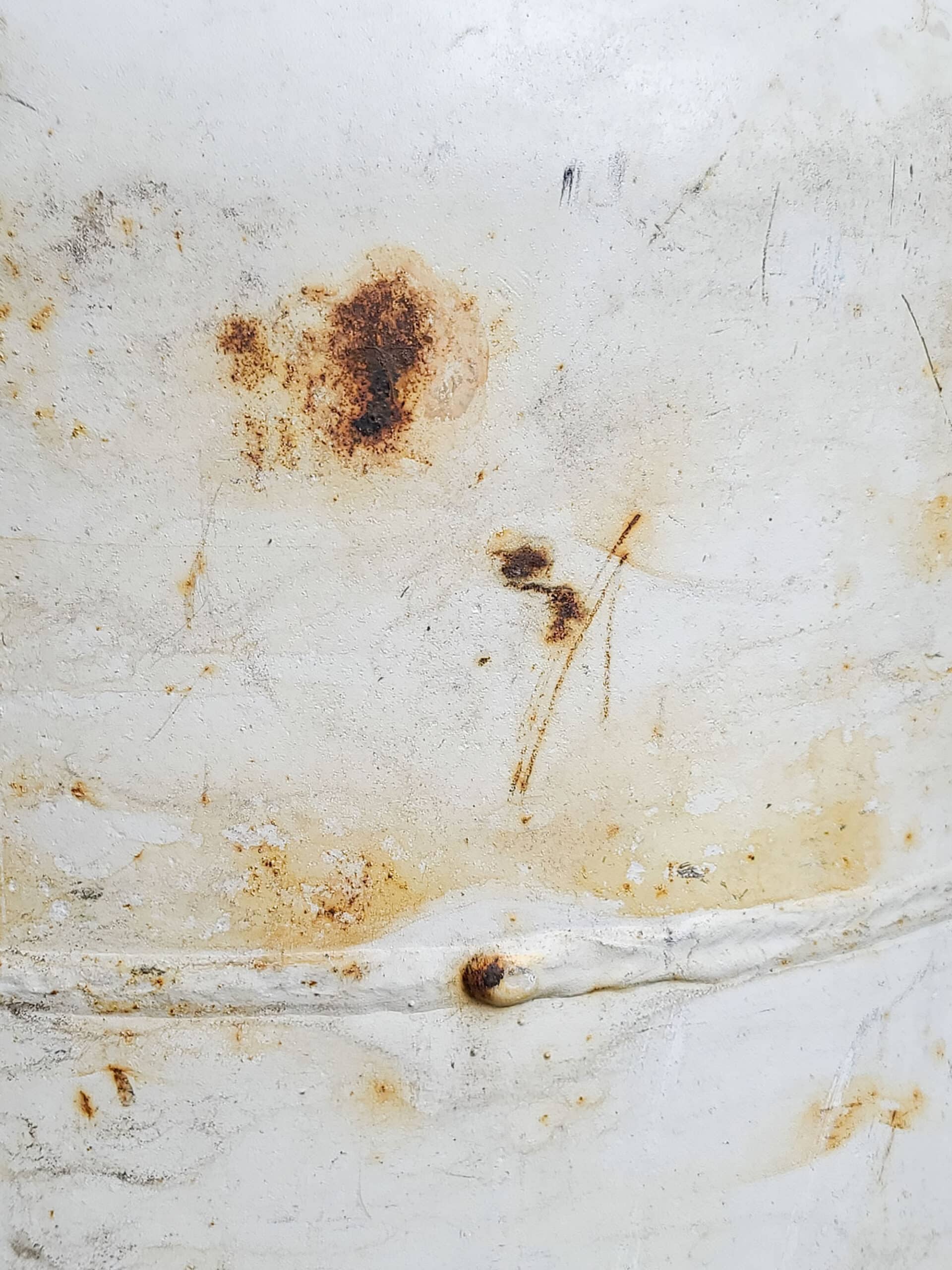A side view of a white barbecue propane tank.  Some surface rust is seen.