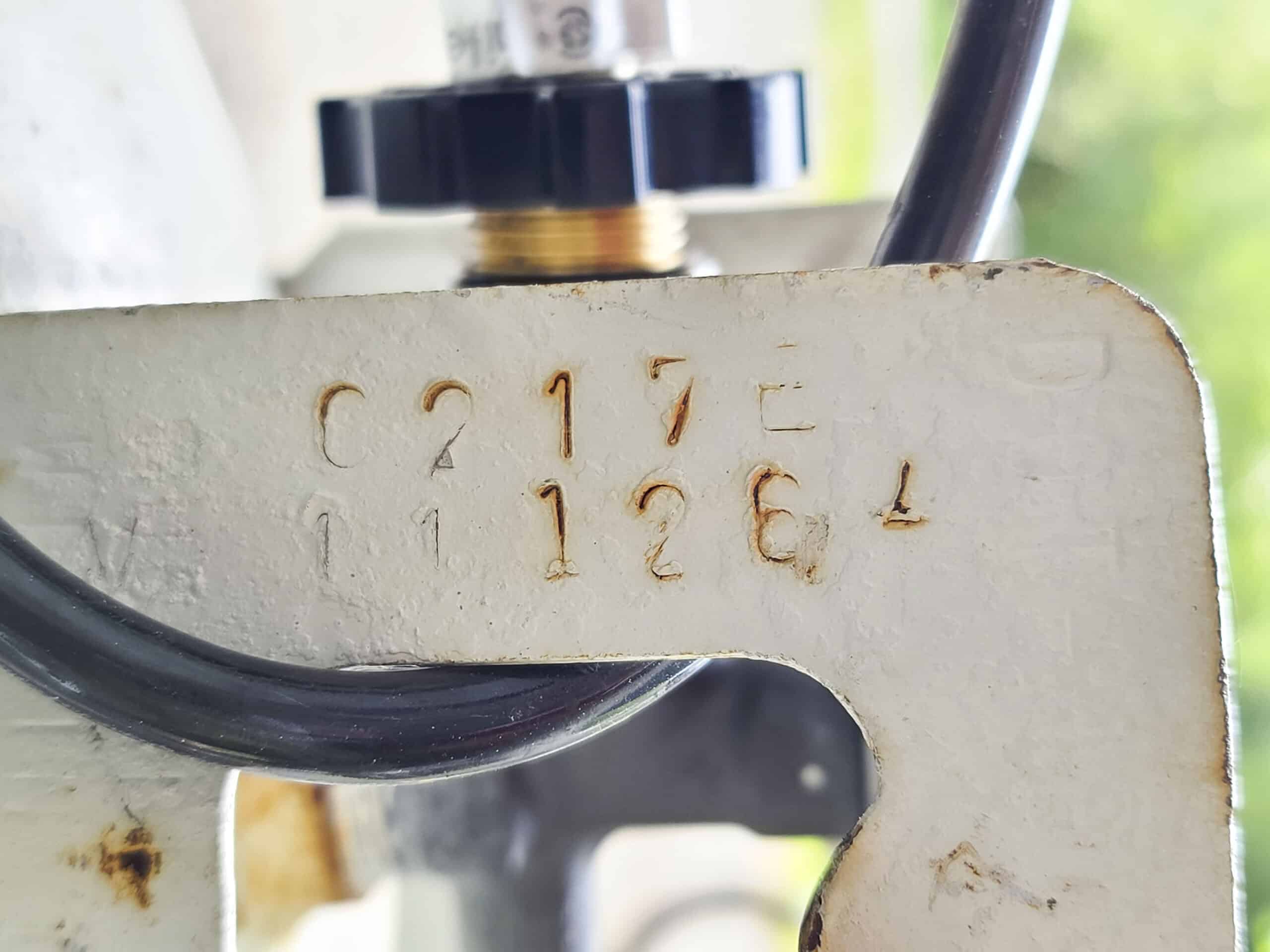 The handle of a white barbecue propane tank.  0217E is stamped on the handle.