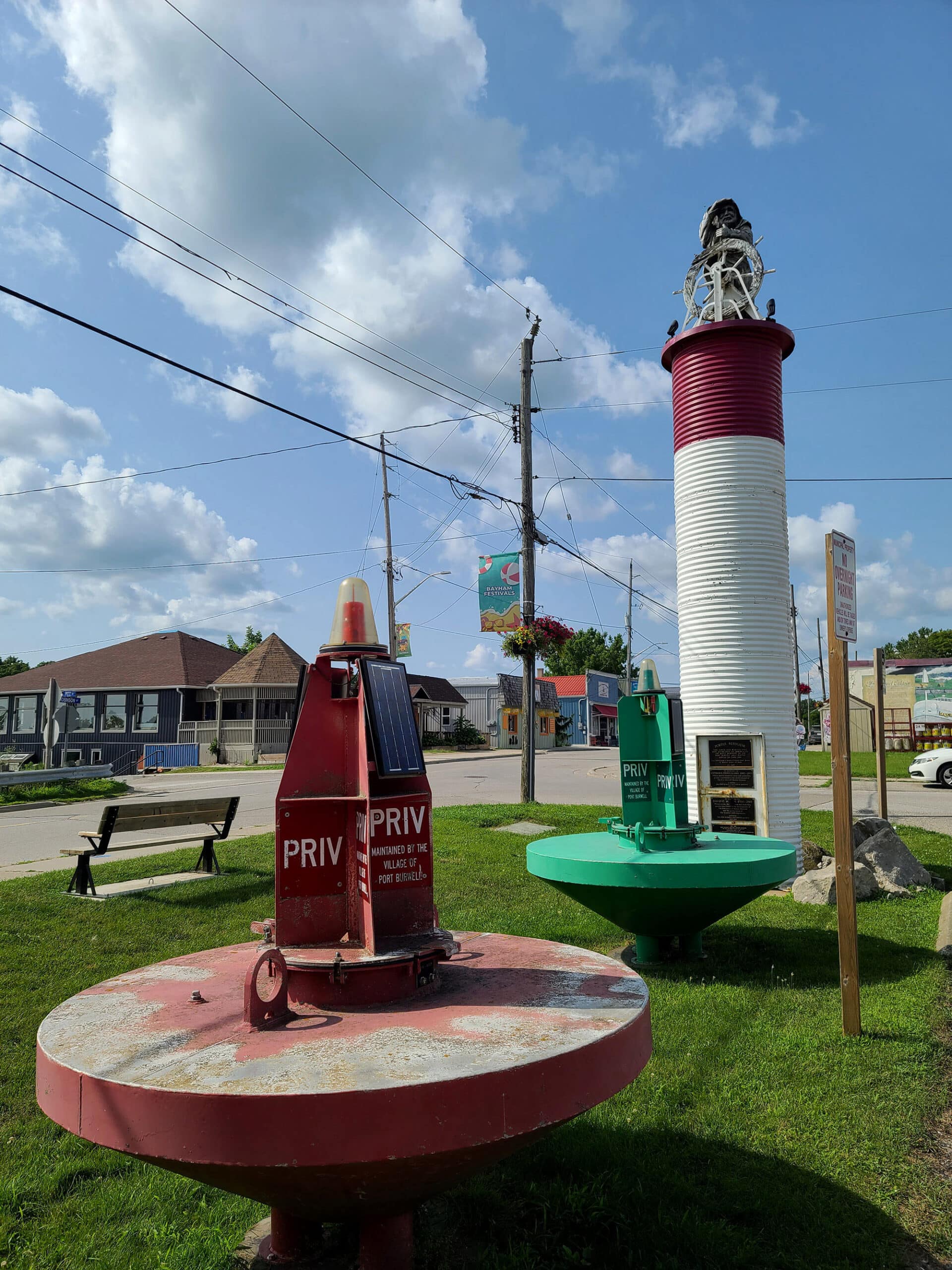 A lighthouse in the background, with 2 large bouys in the foreground. This is a display at the Port Burwell Marine Museum.