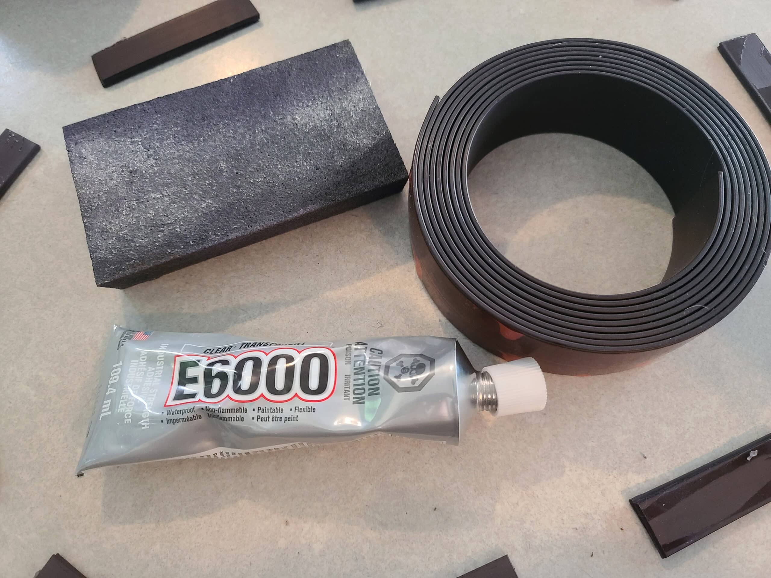 A sandpaper block, a roll of magnet strip, and a tube of E-6000 glue.