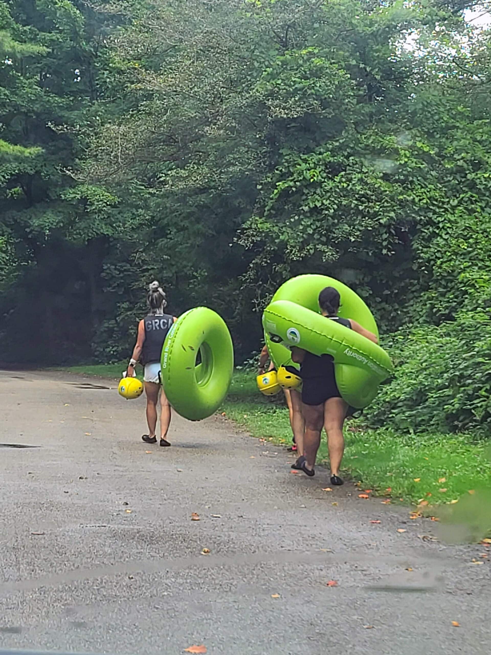 Several people carrying bright green inner tubes, walking away from the photographer.