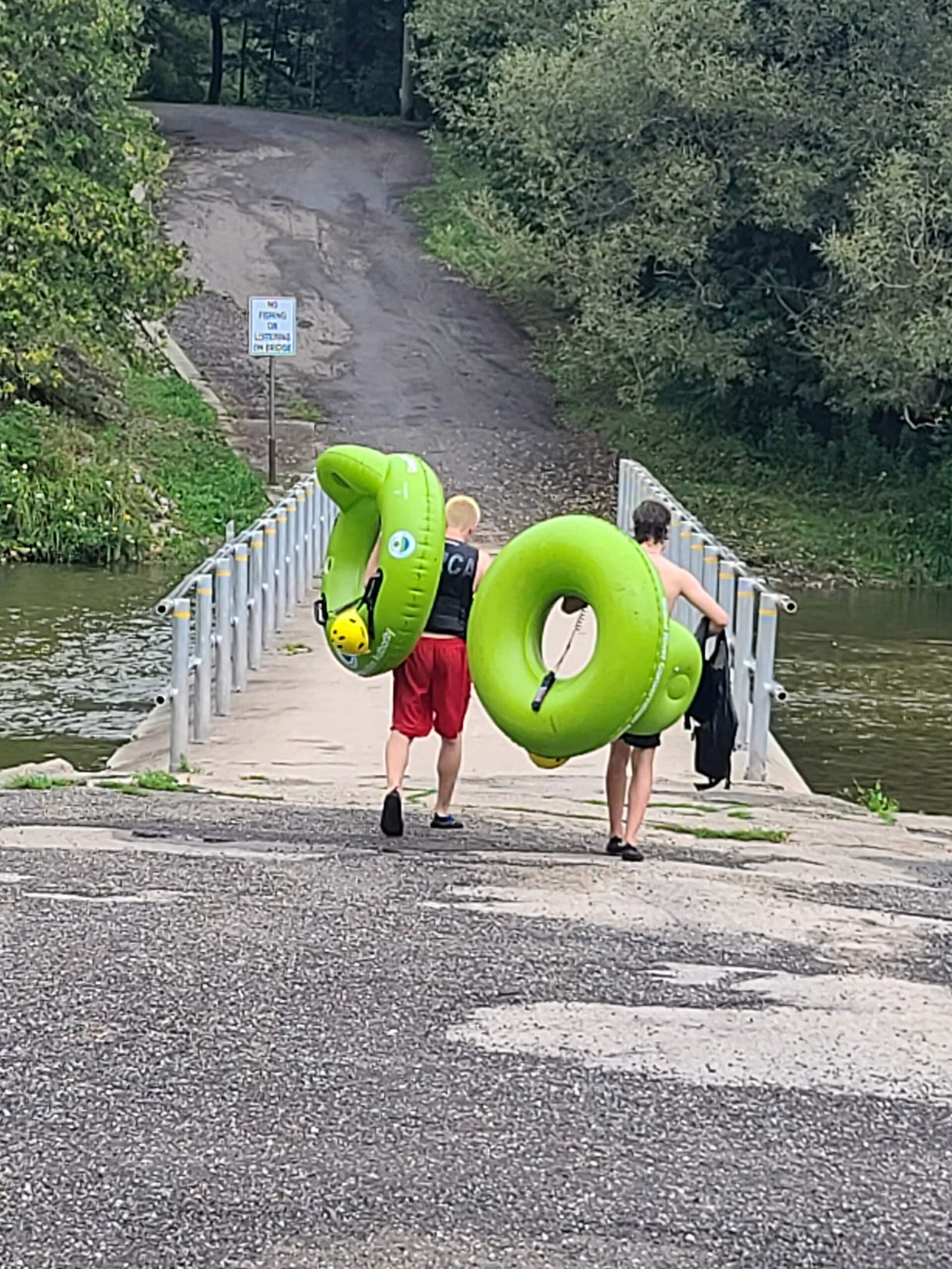 Several people carrying bright green inner tubes, walking away from the photographer.