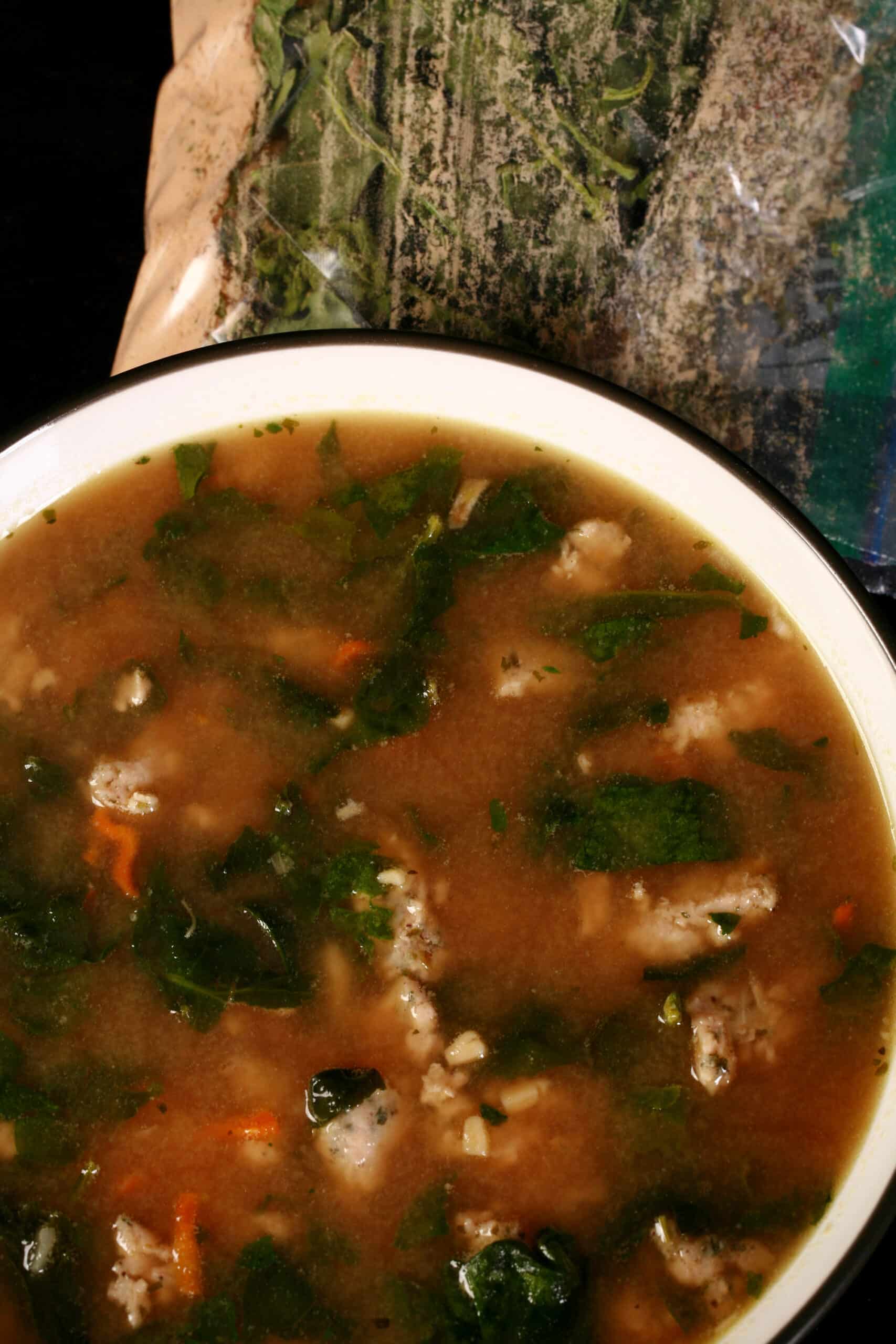 A bowl of gluten free soup next to a baggie of keto italian wedding soup mix.