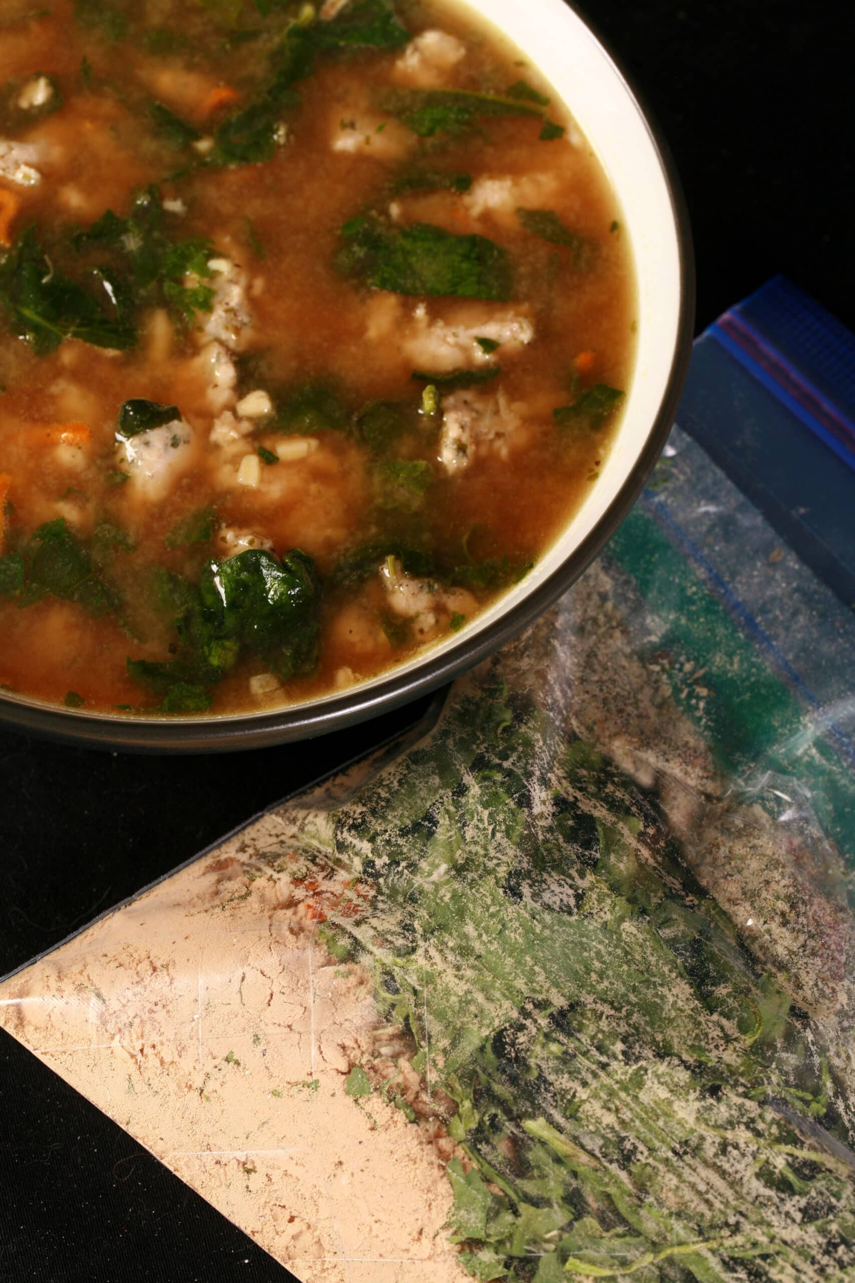 A bowl of soup next to a baggie of gluten free italian wedding soup mix.