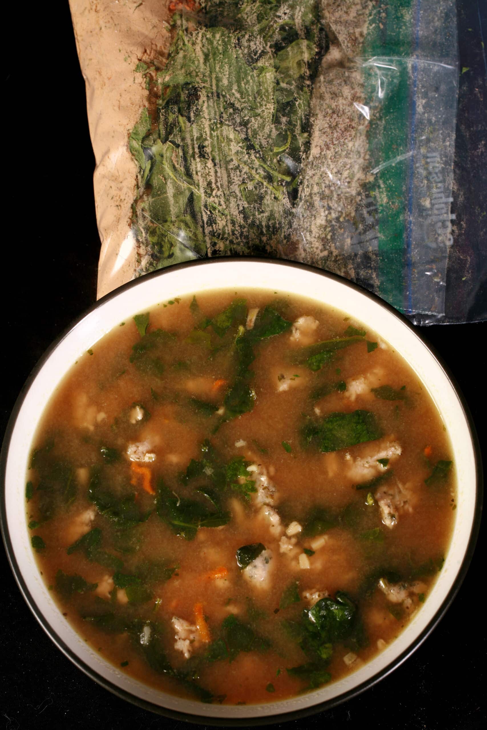 A bowl of gluten free soup next to a baggie of keto italian wedding soup mix.