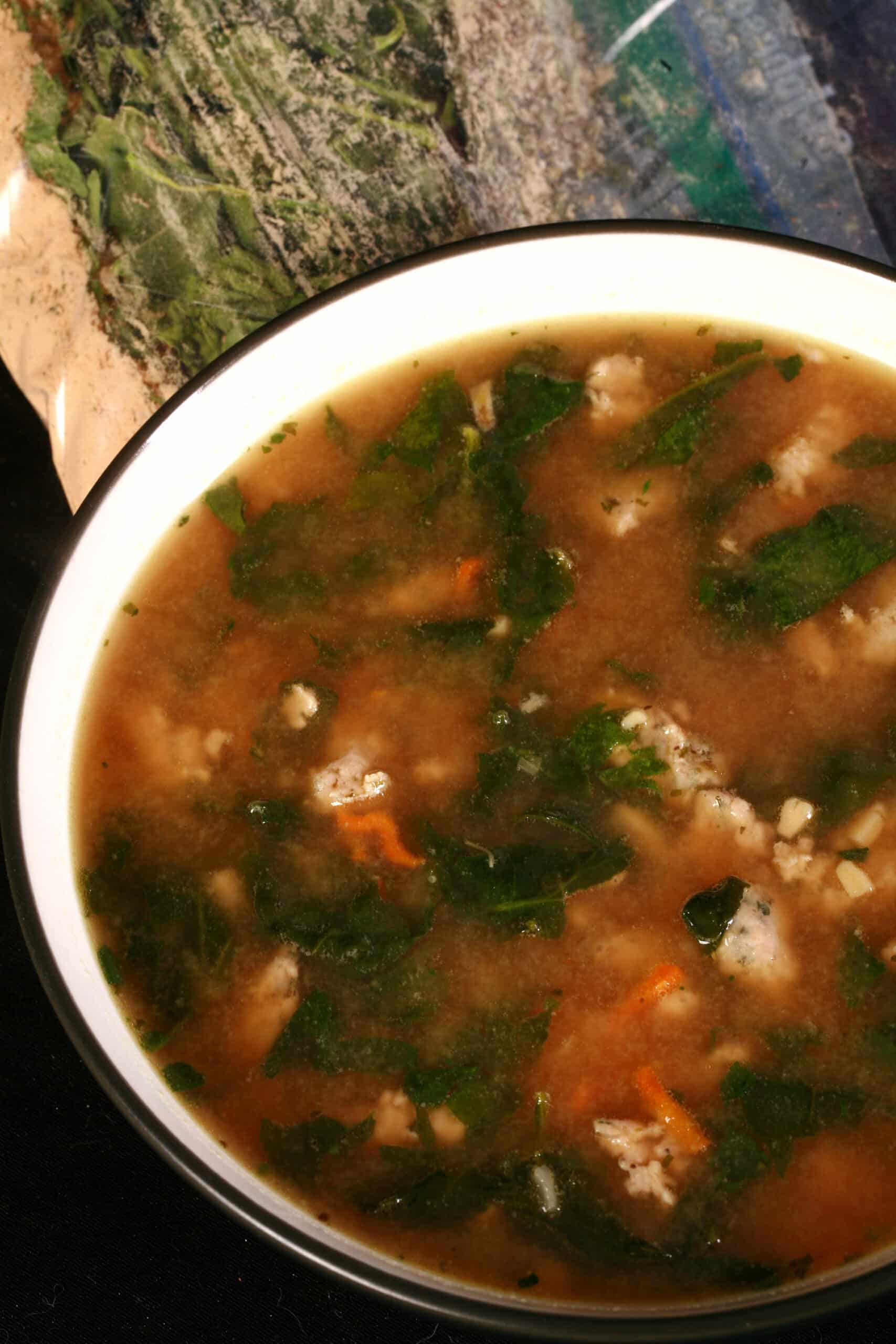 A bowl of soup next to a baggie of gluten free italian wedding soup mix.