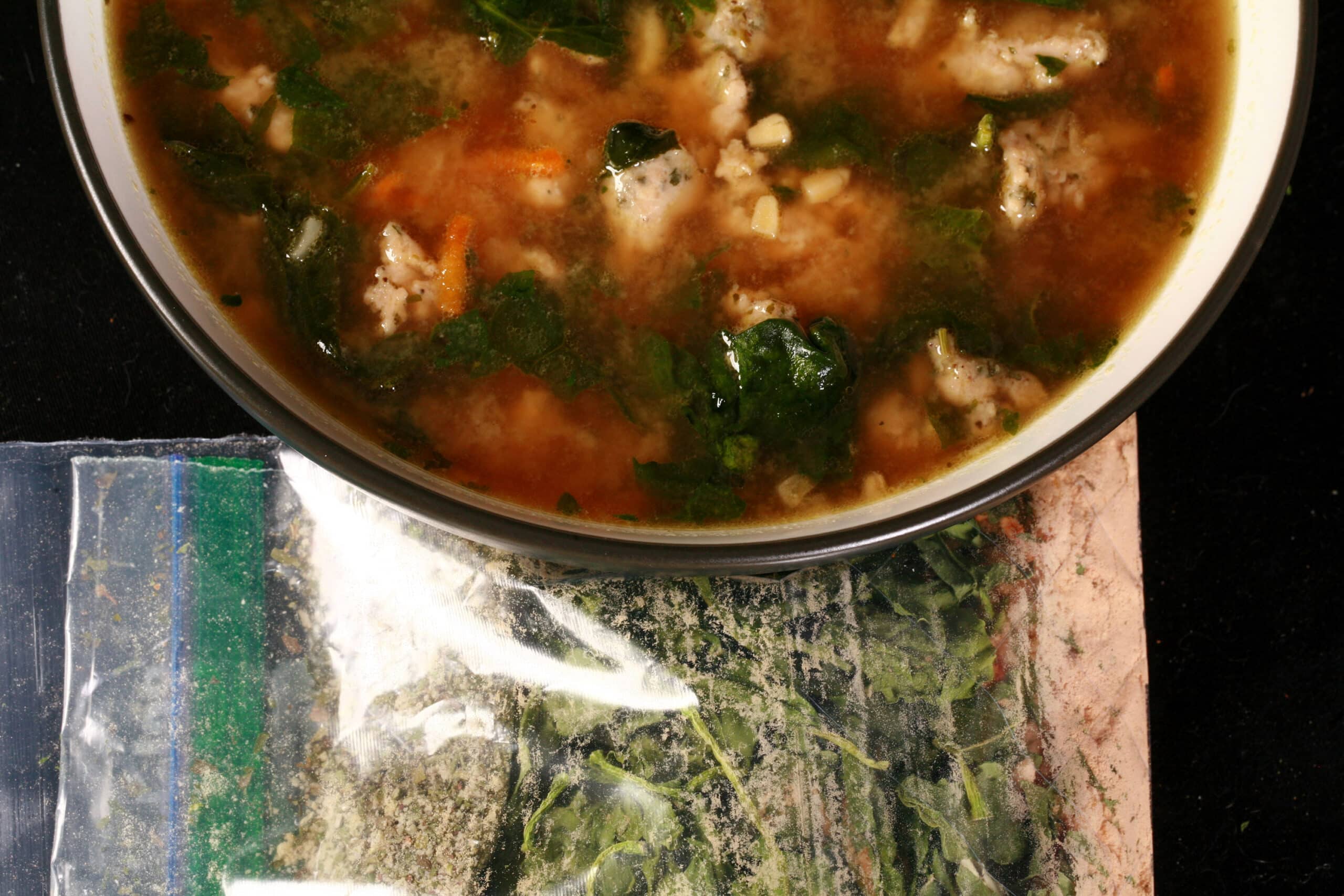 A bowl of gluten free soup next to a baggie of keto italian wedding soup mix.