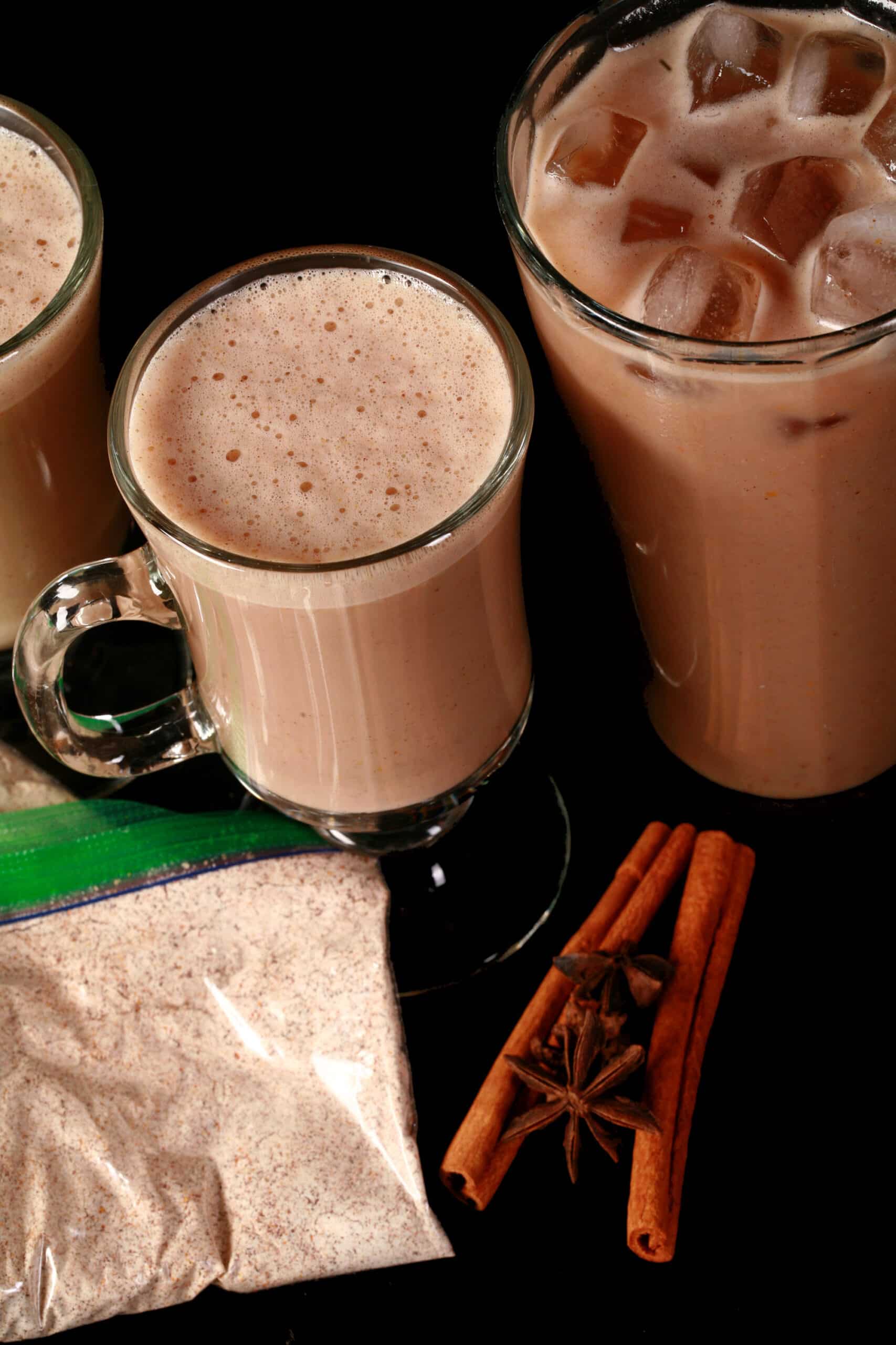 2 mugs of protein pumpkin chai latte, a tall glass of protein powder iced pumpkin chai latte, and several bags of mix.