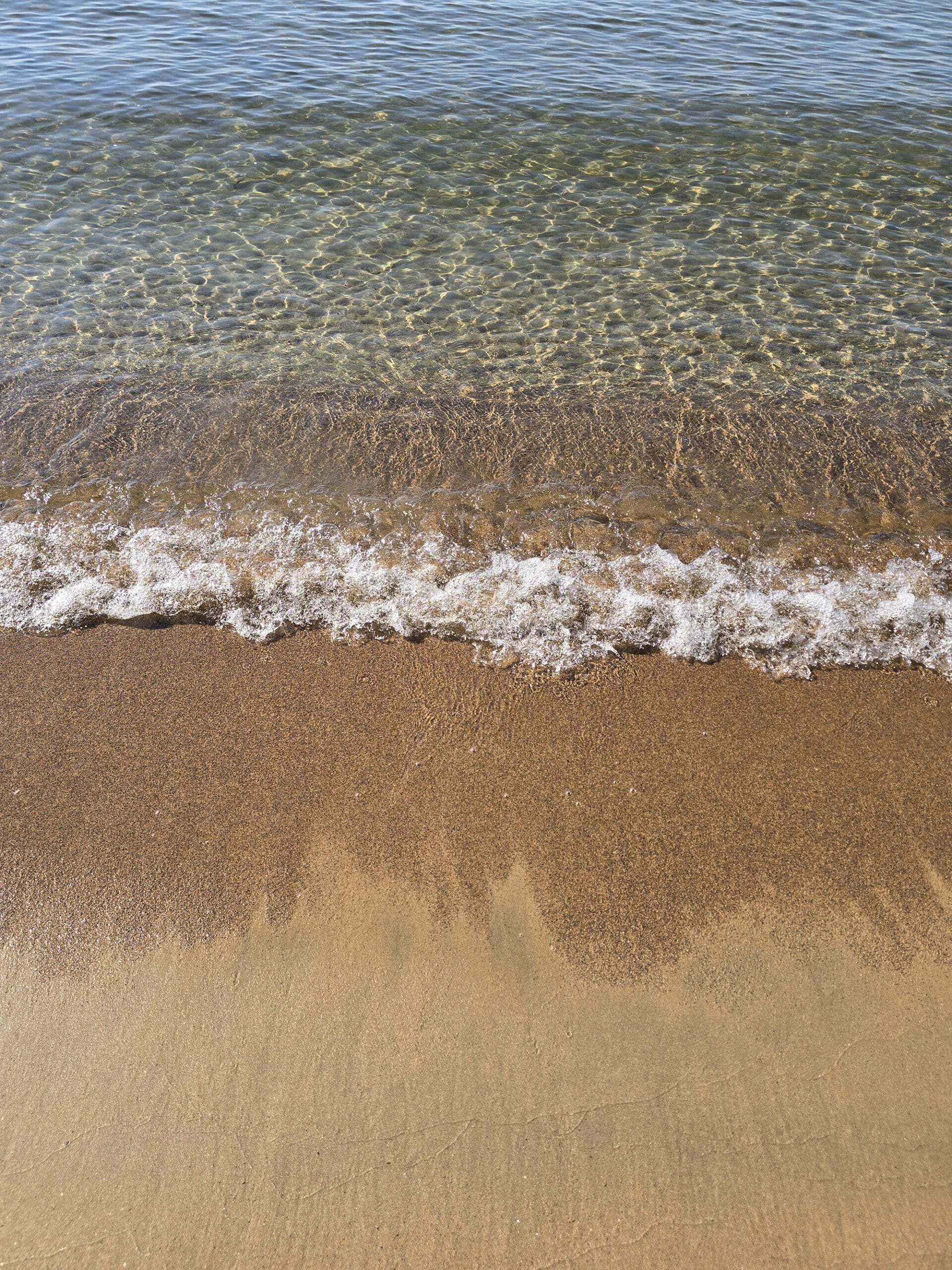 The clear water of lake superior rolling up on a sandy beach.