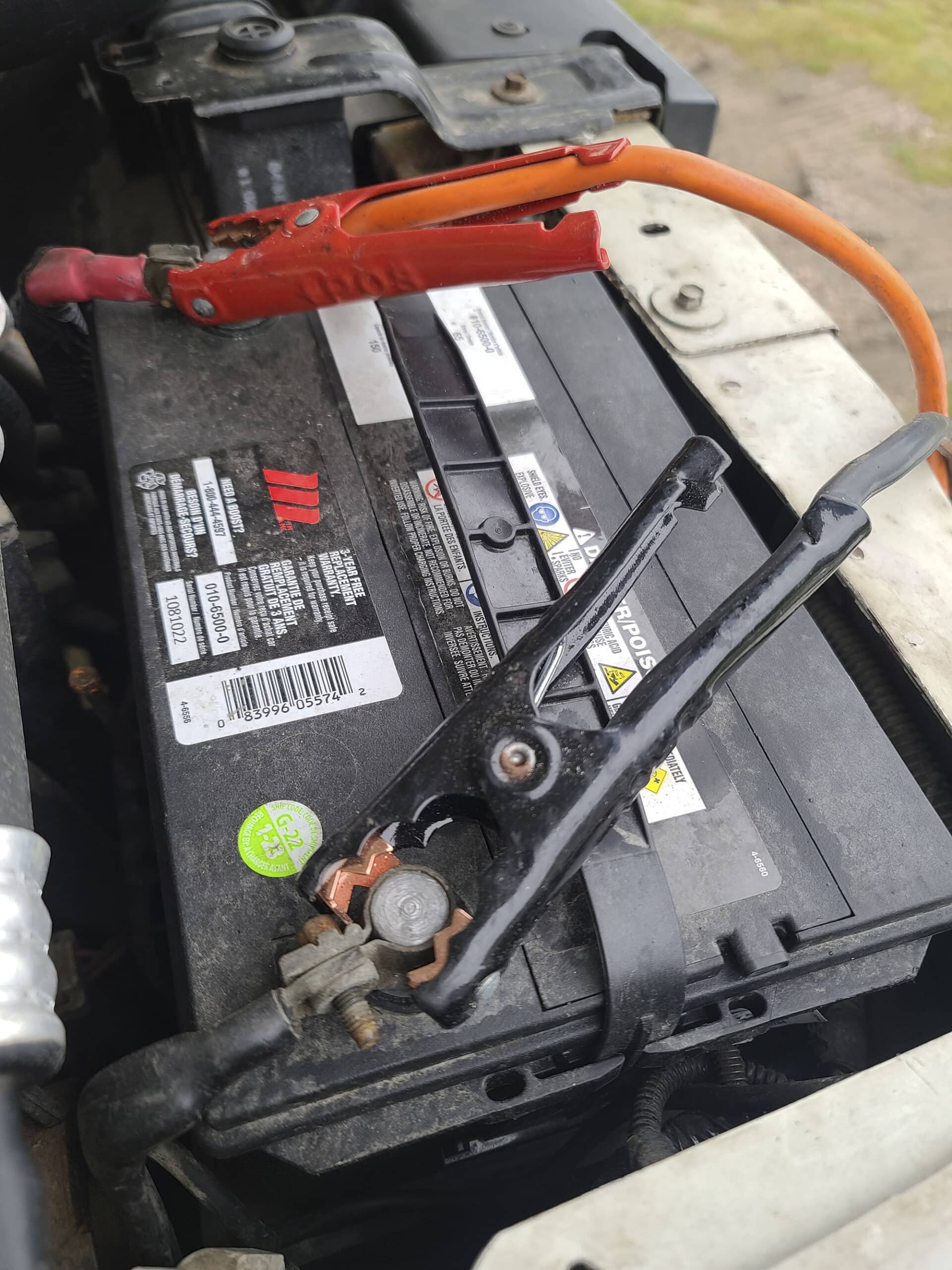 Under the hood of a motorhome, focused on the battery.  Jumper cables are attached to the terminals of the battery.