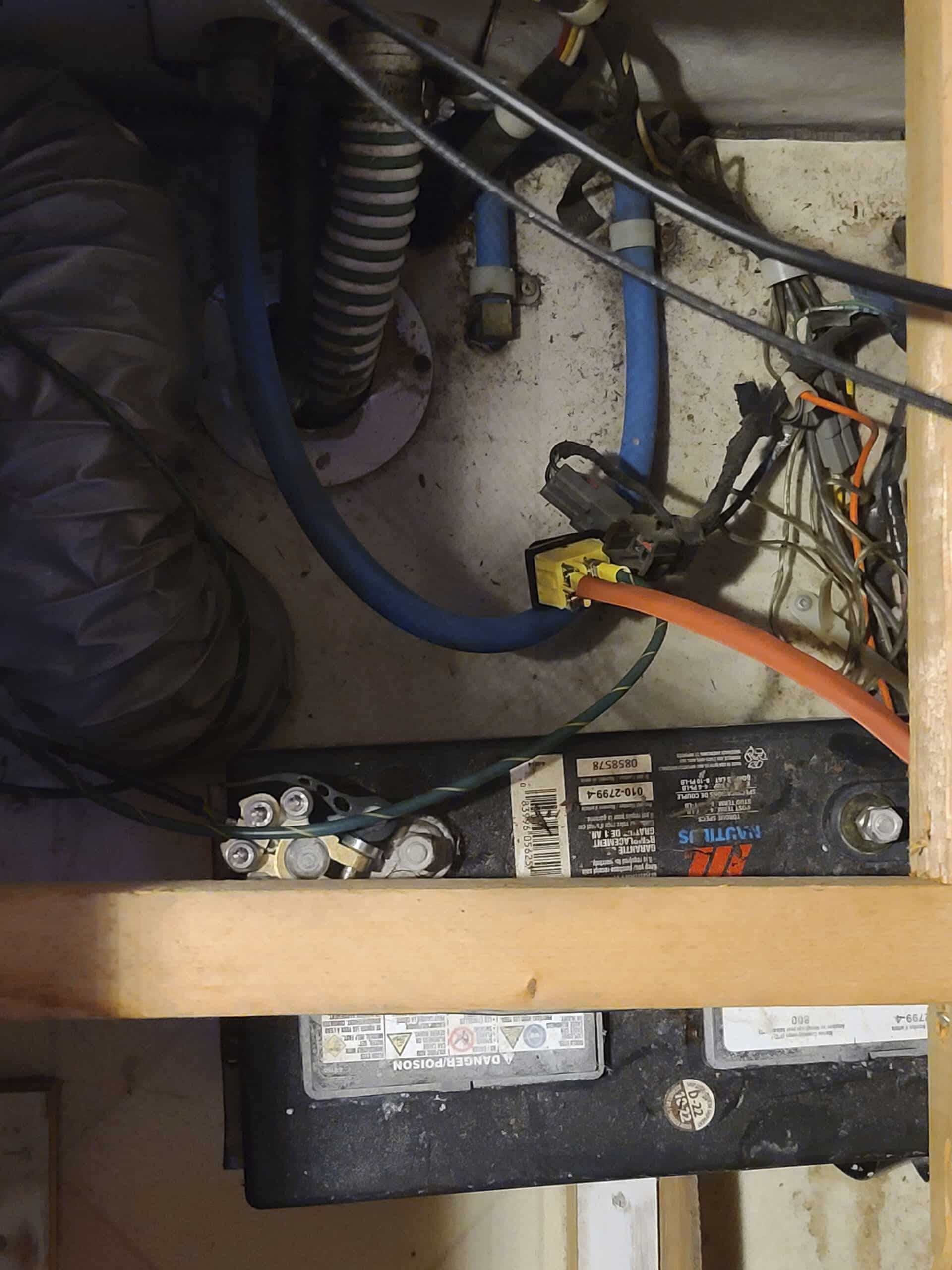 Under the seat of a motorhome, hoses and wires are seen, along with a deep cycle 12v battery.