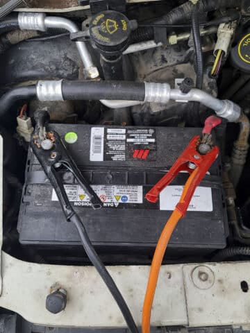 A look under the hood of a motorhome, focused on the battery. Jumper cables are attached to each terminal of the battery.