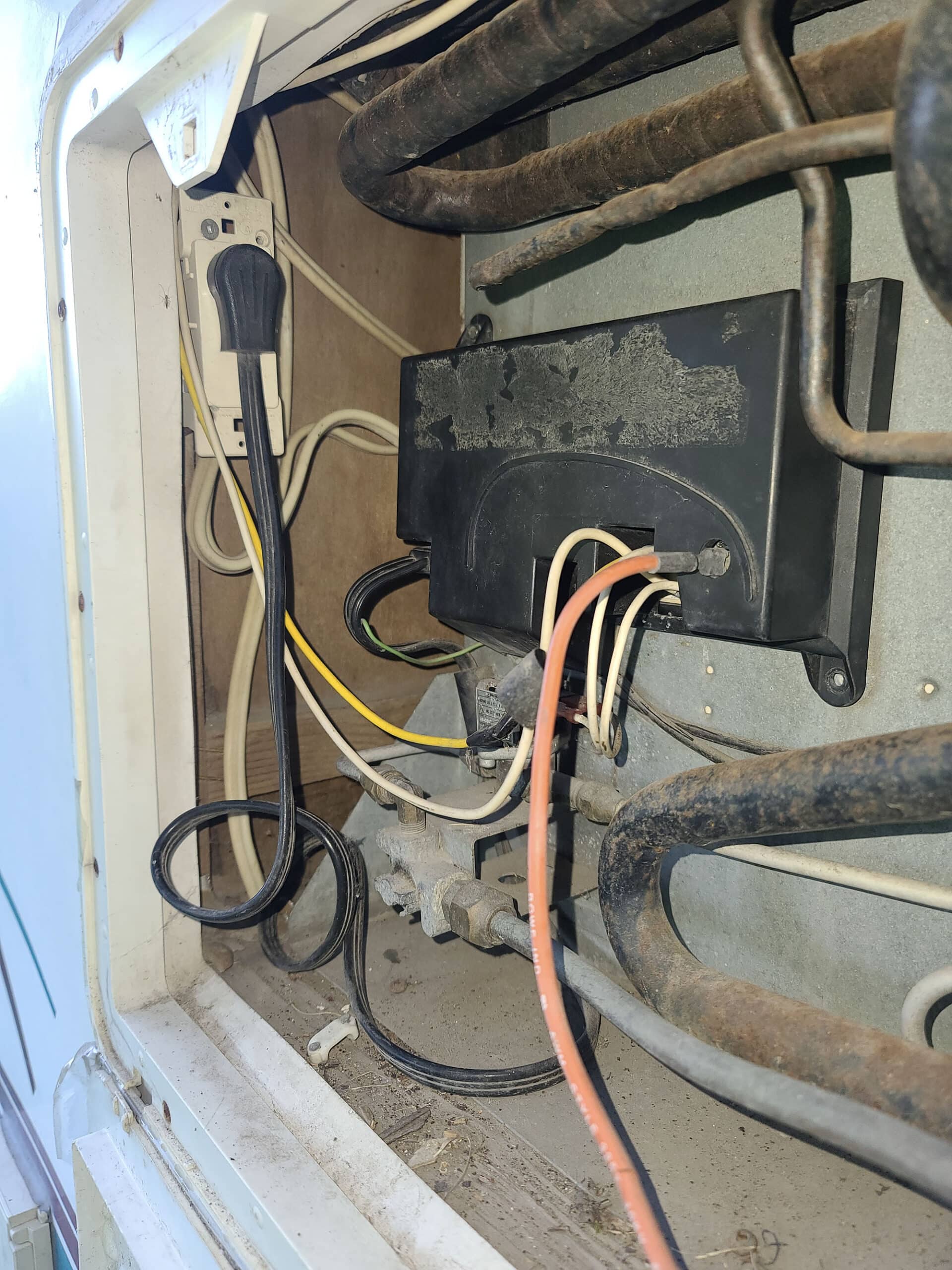 The outside of an RV motorhome, looking in the cabinet for the fridge.  An AC outlet and various wires can be seen.