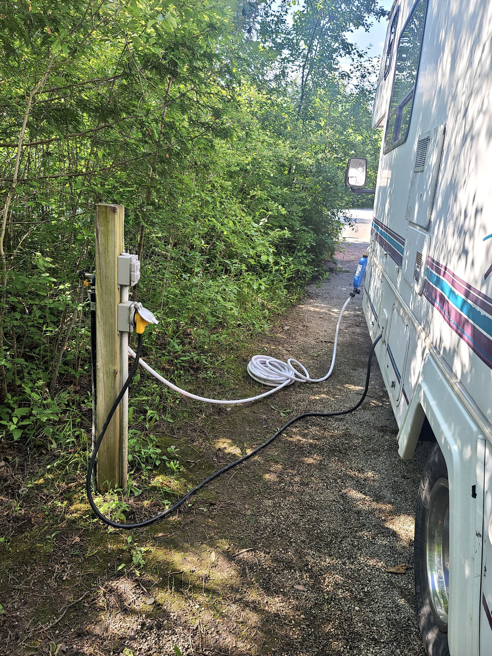 The back side of a motorhome, next to a post with power and water hookups.  A cord and hose are seen connected.