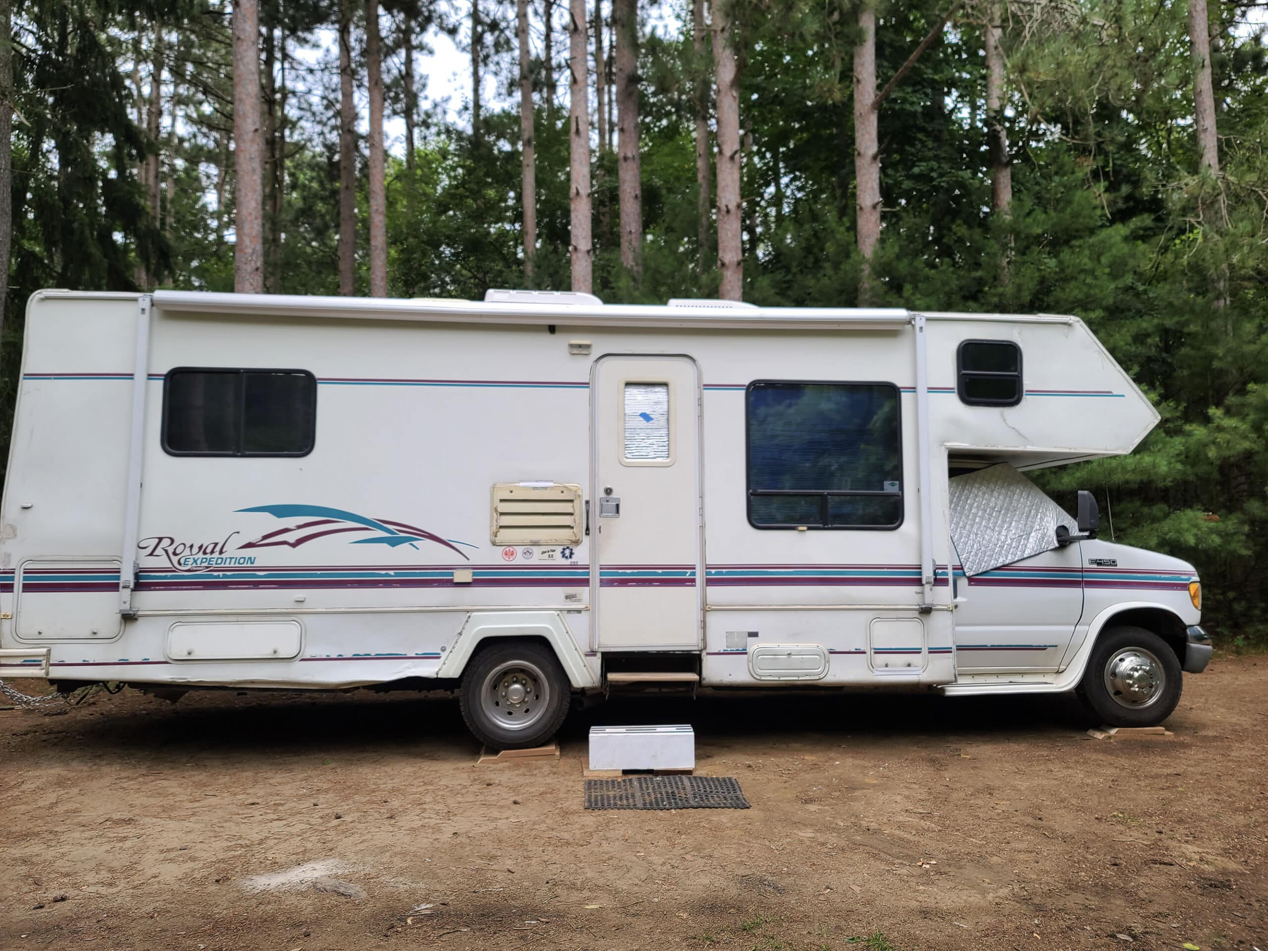 A side view of a motorhome at a campsite.  There are boards seen under the tires.  The side steps are out, but the awning is retracted.