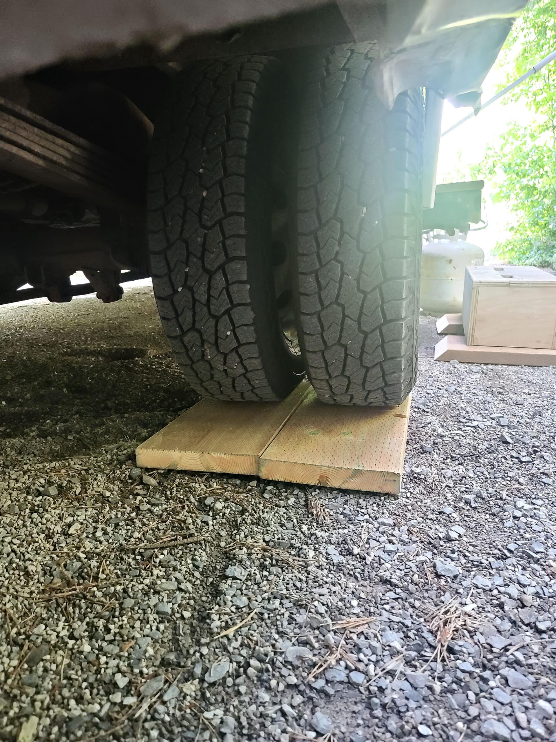 A low view under a motorhome looking at the dual rear tires.  Under each tire is a 2x10 board.