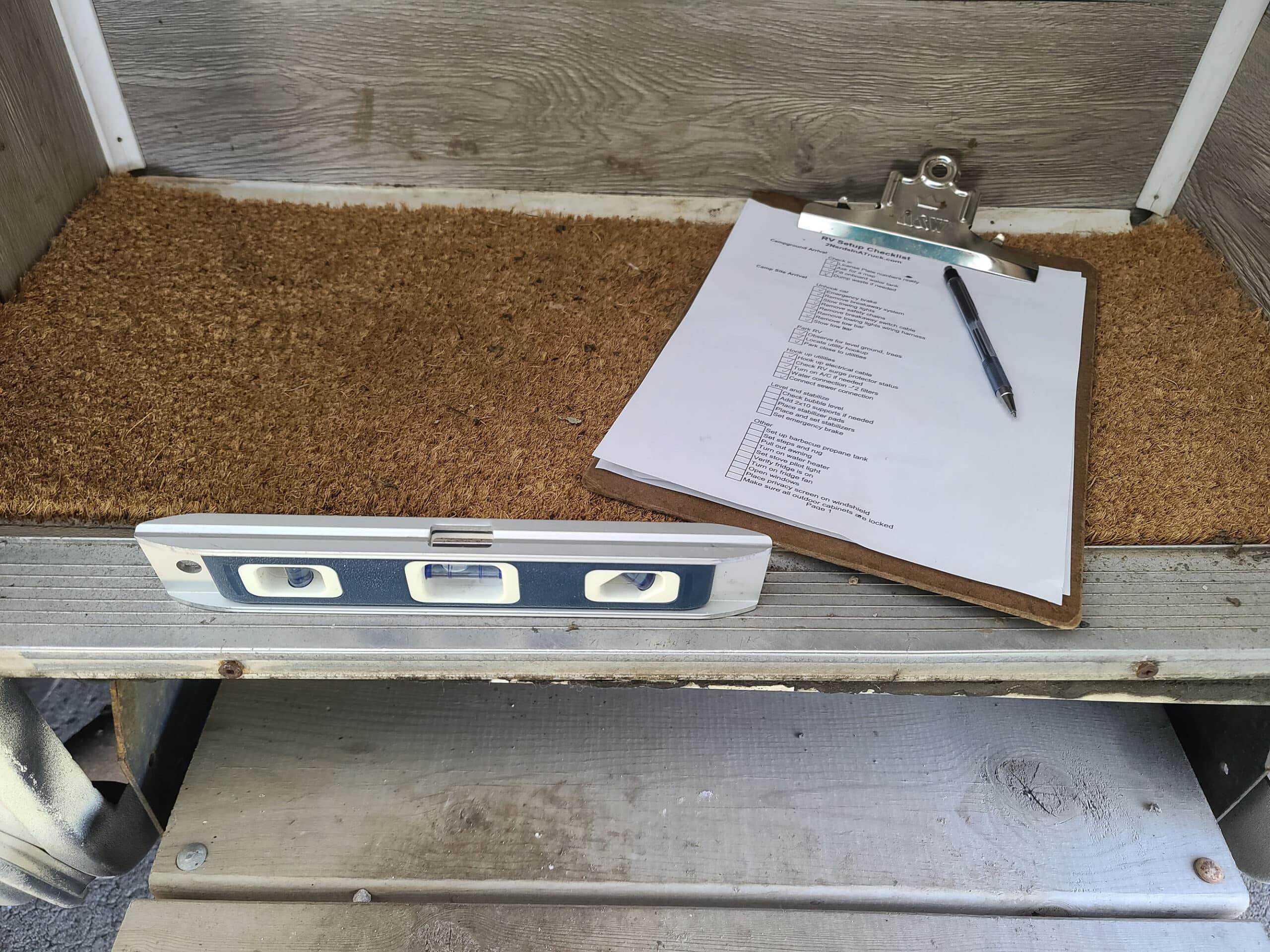 A clipboard with a paper checklist and pen, sitting on a step of an RV.  There is a small level on the floor of the RV.