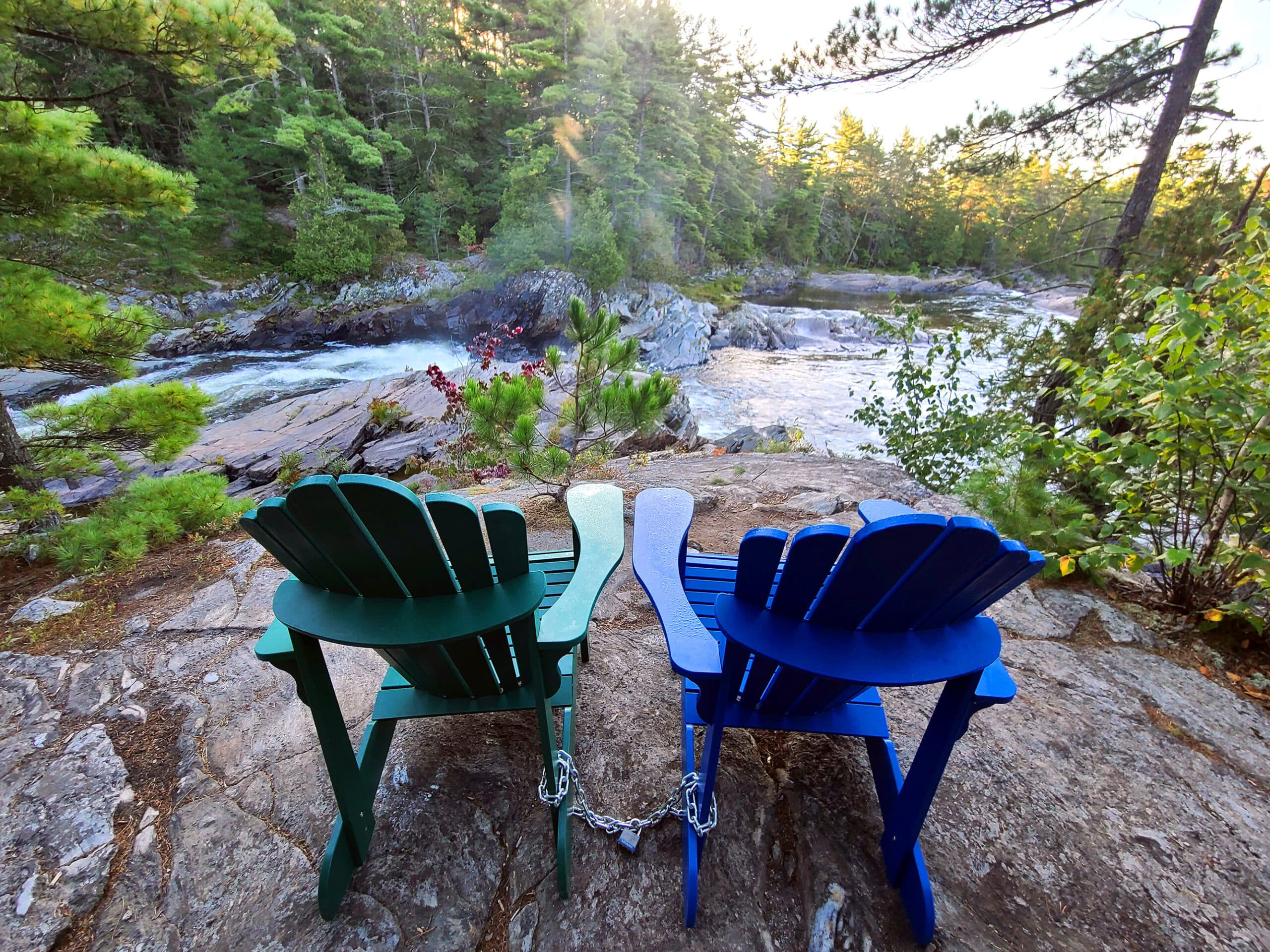A green and a blue muskoka chair overlooking the rapids.