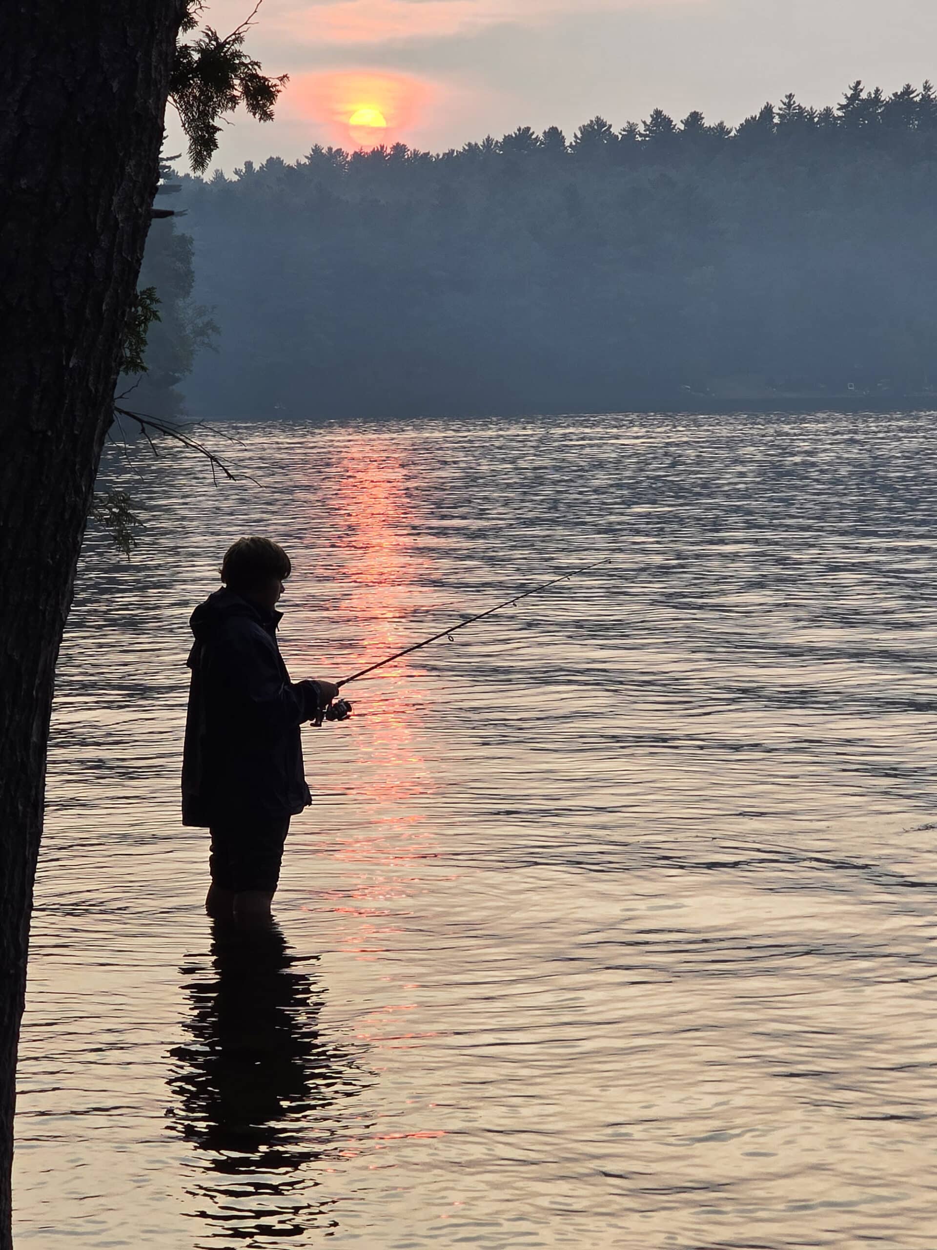 Someone fishing in front of a sunset on Mazinaw Lake.