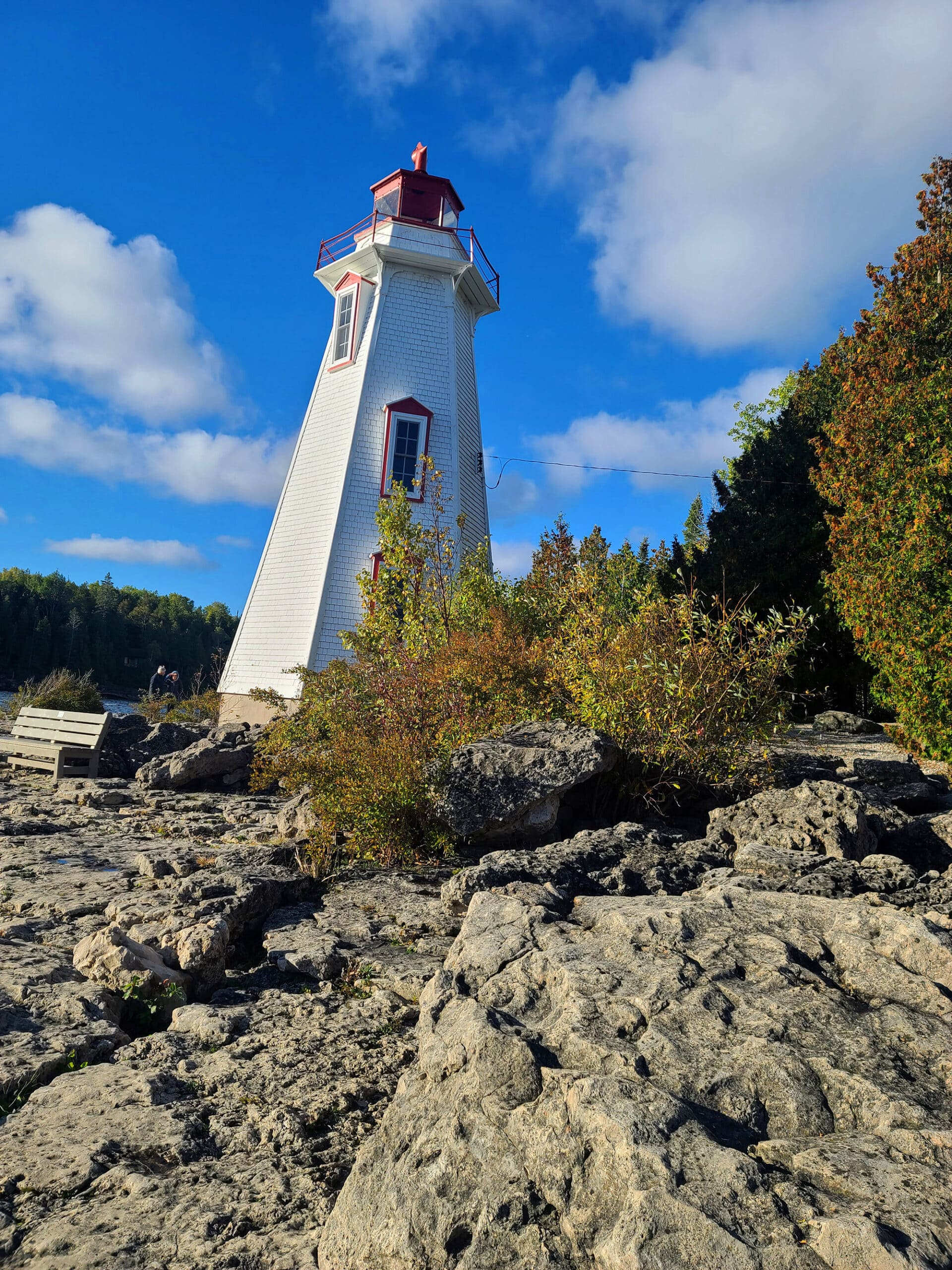 A tall lighthouse with a rocky shore in front of it, in Tobermory.